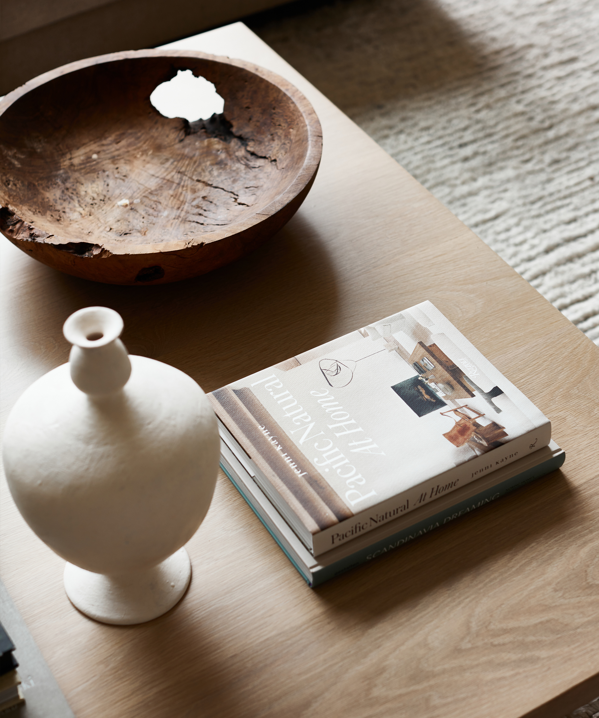 wood coffee table with coffee table books a white vase and wood decorative bowl