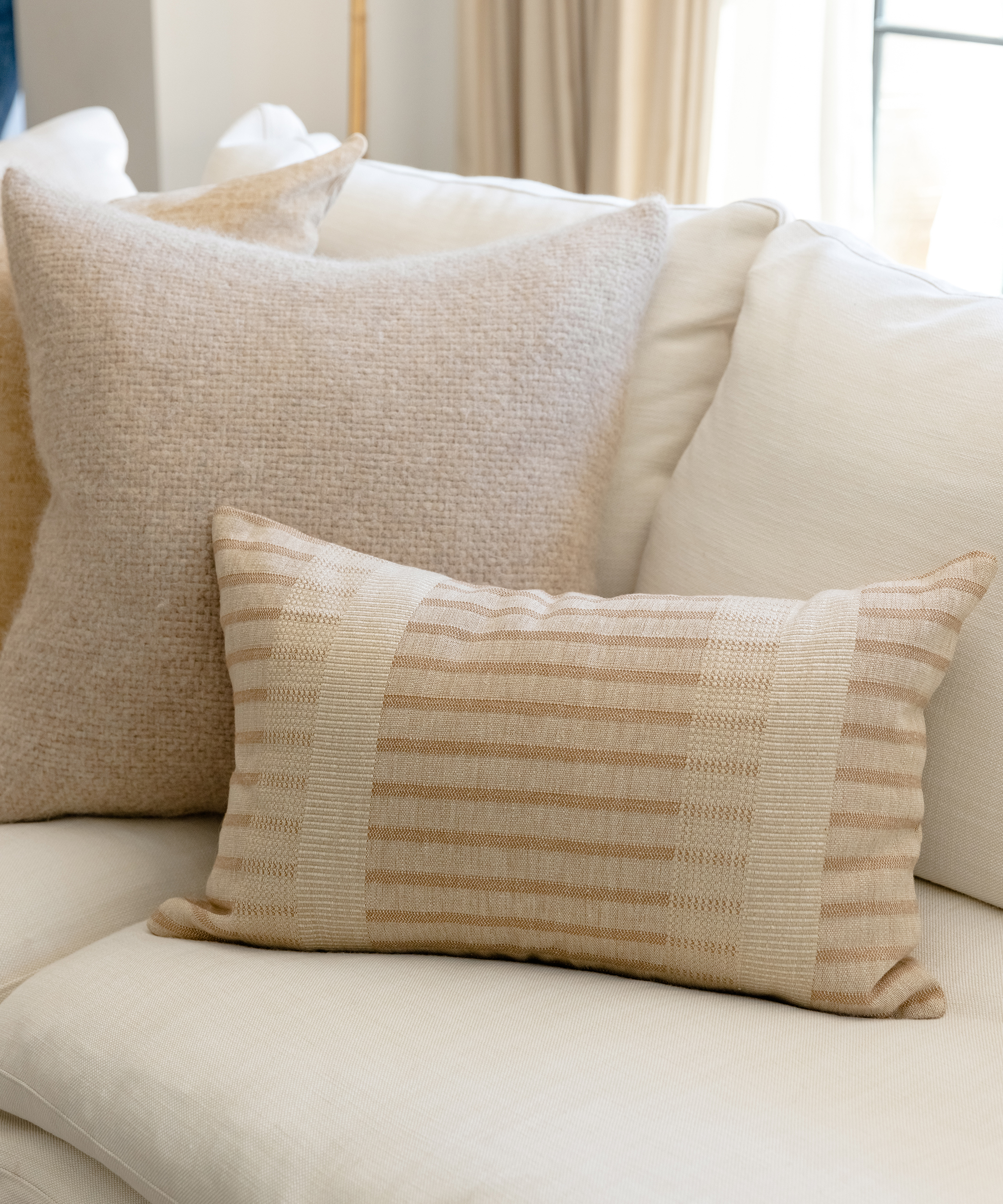 two accent pillows on a white couch, one striped pillow and one taupe alpaca pillow