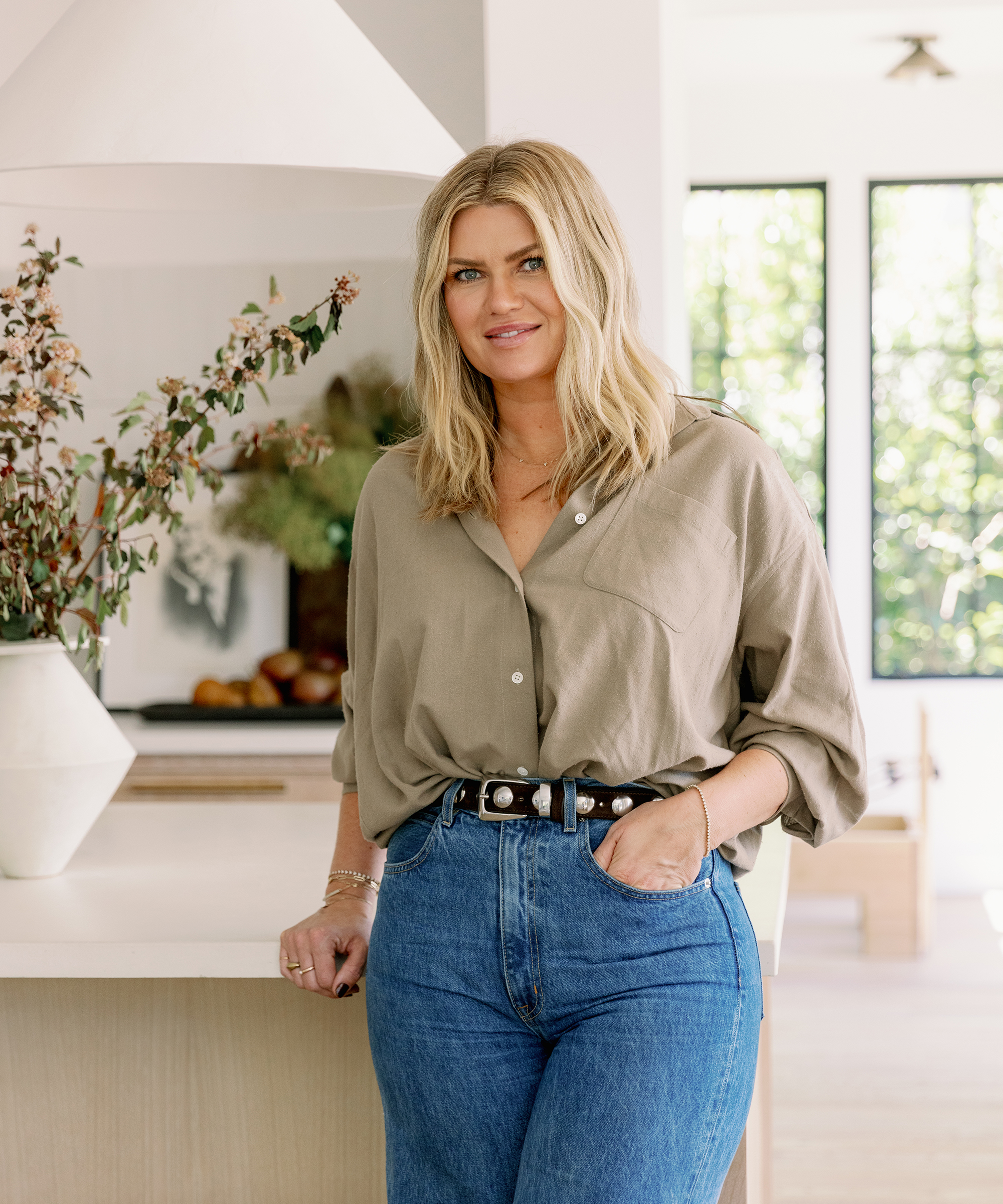 nicole green standing in a white kitchen with a relaxed oversized button down shirt in hazel and blue jeans