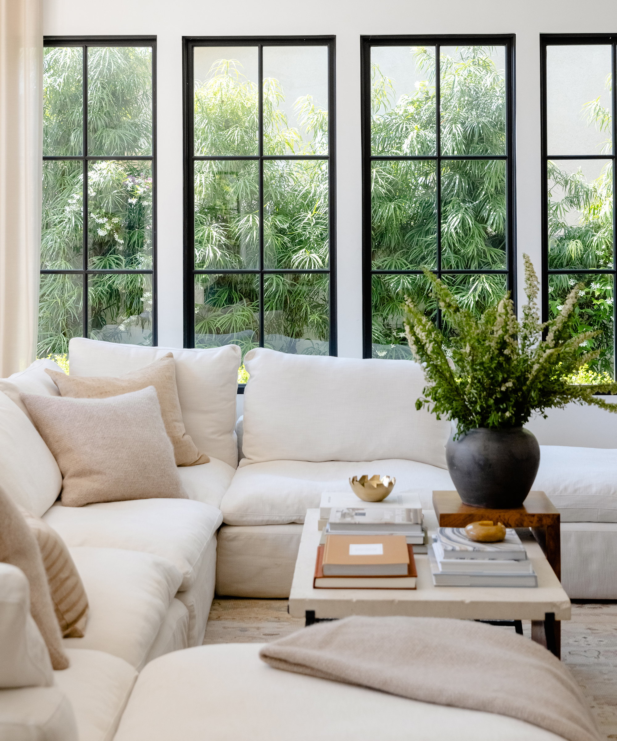 white sectional couch with taupe accent pillows and a marble top coffee table with a black vase and green plants
