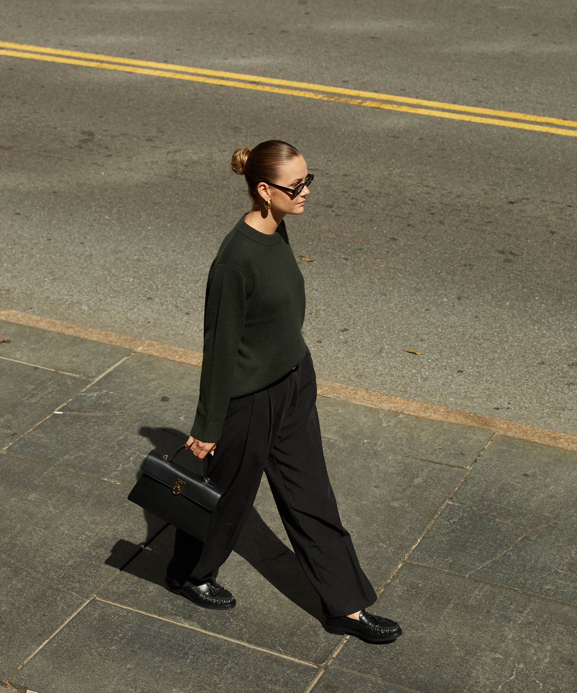 kristel walking in on a sidewalk in a forest green sweater and black trousers and black loafers