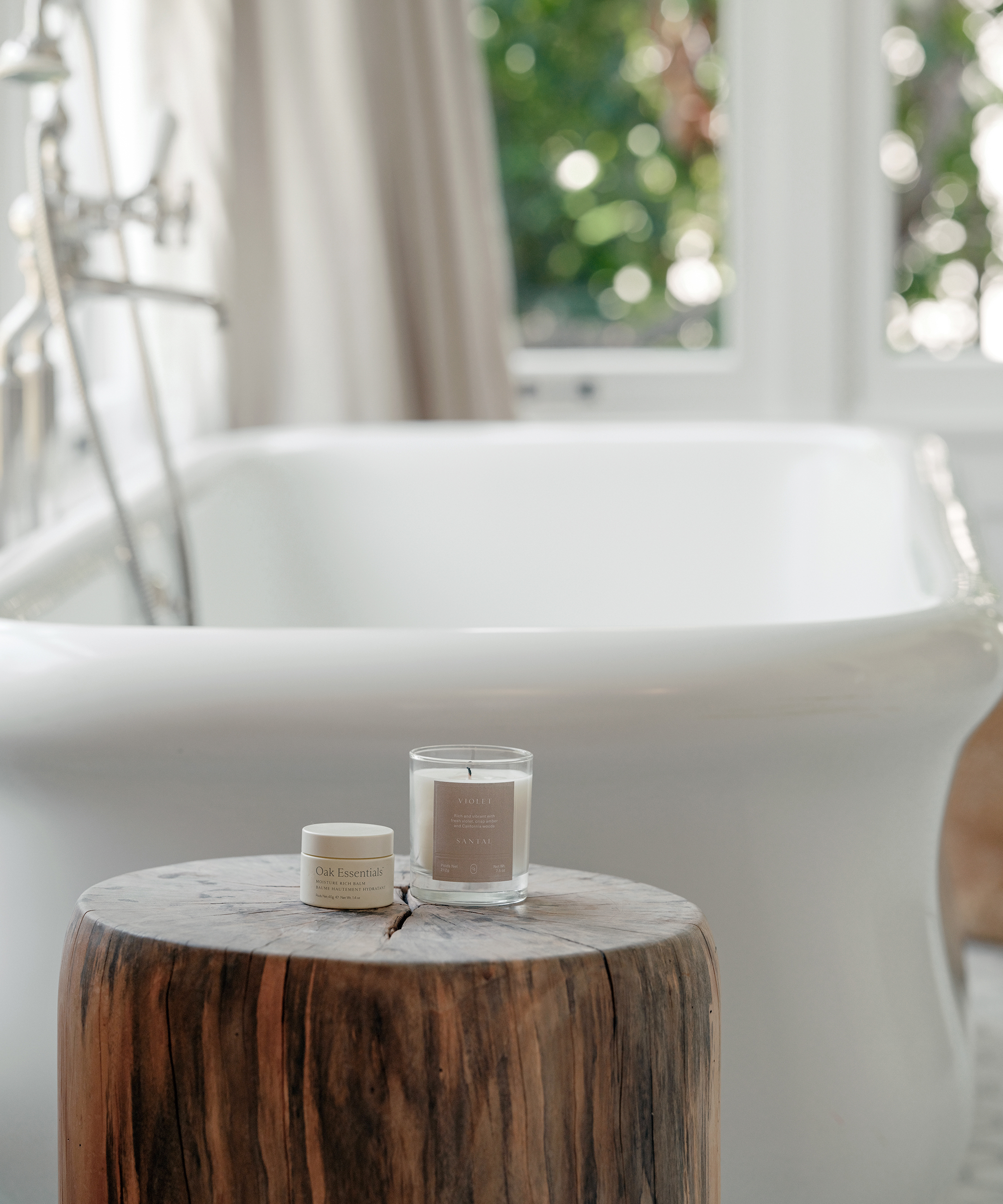 oak essentials candle and balm on a wood stump next to a bathtub