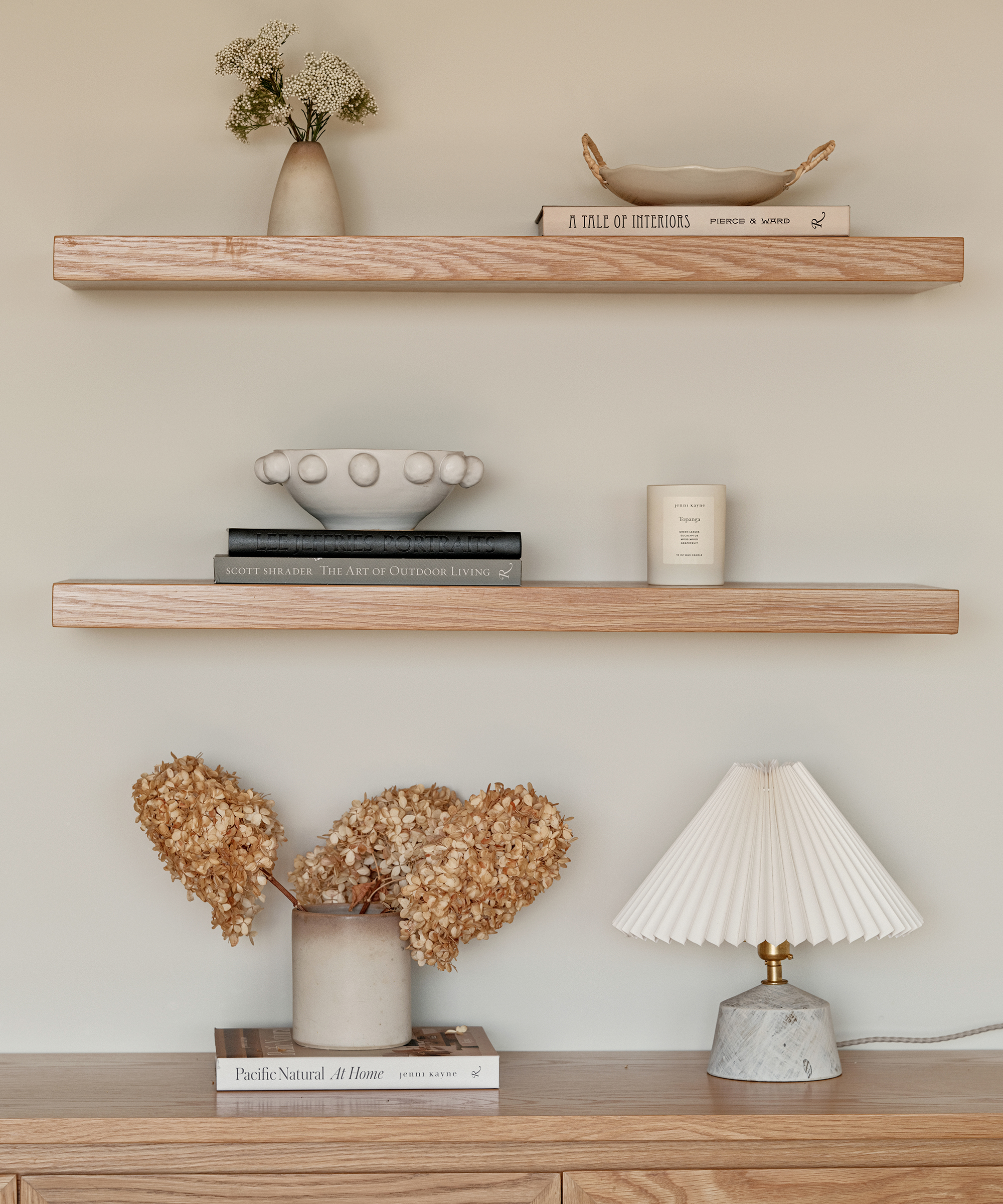 open wood shelving with decorative accents, flowers a coffee table book and a marble lamp