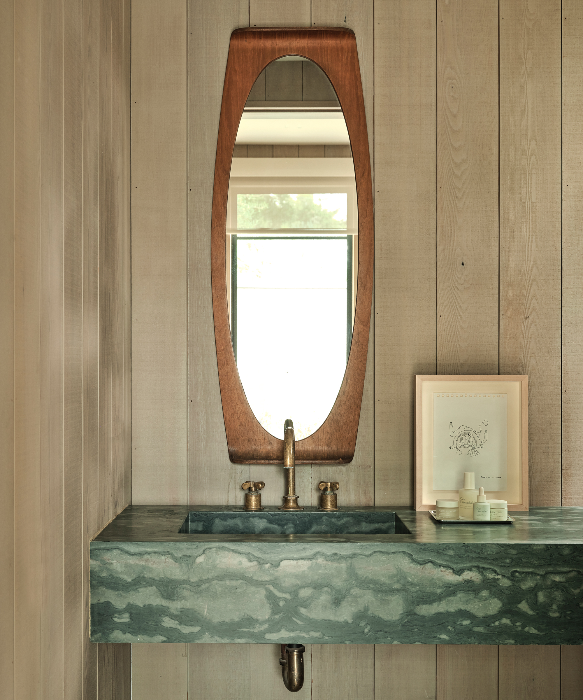 a powder room with oak walls and a green marble sink and a wooden mirror