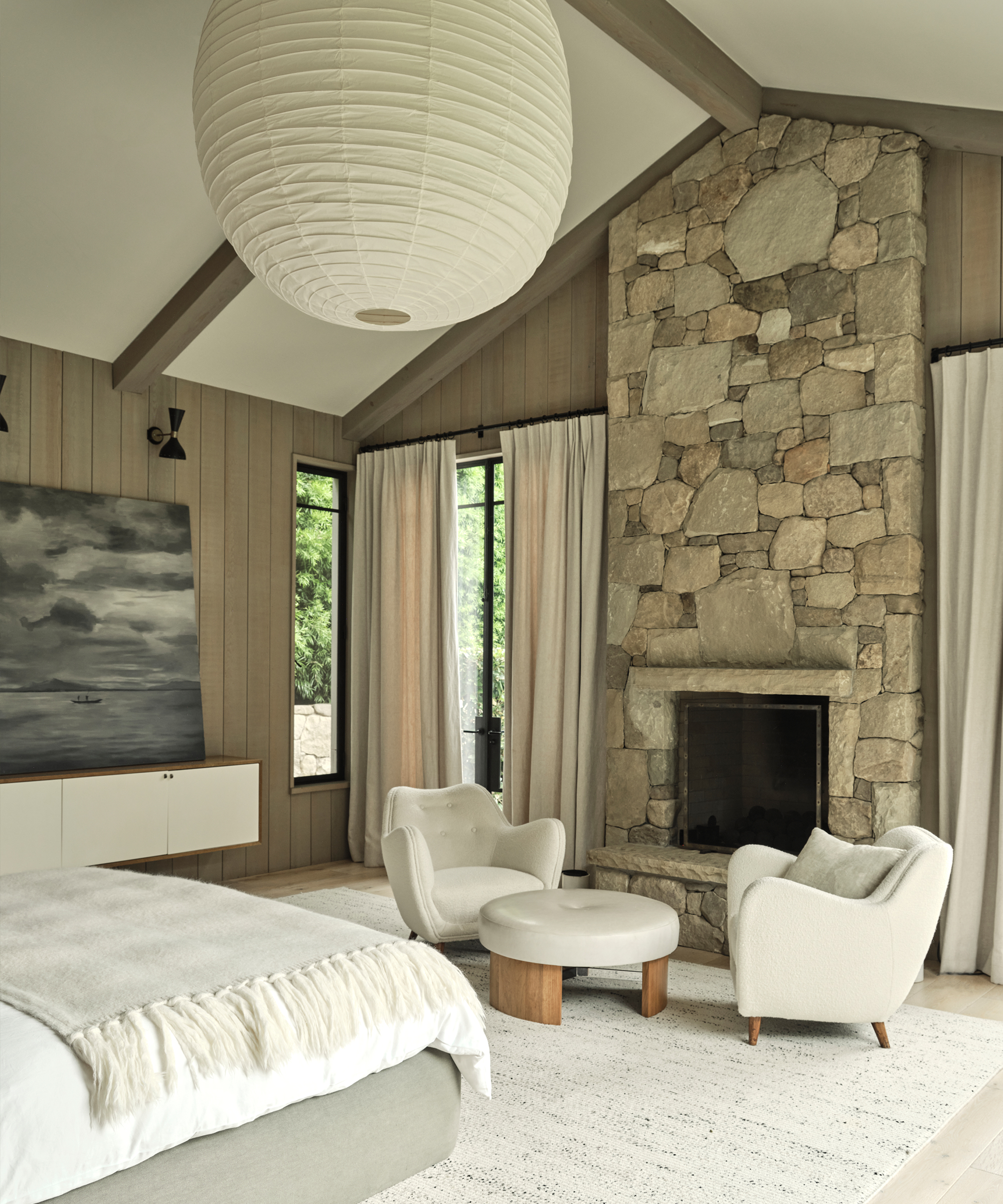 primary bedroom with a stone fireplace and two ivory accent chairs