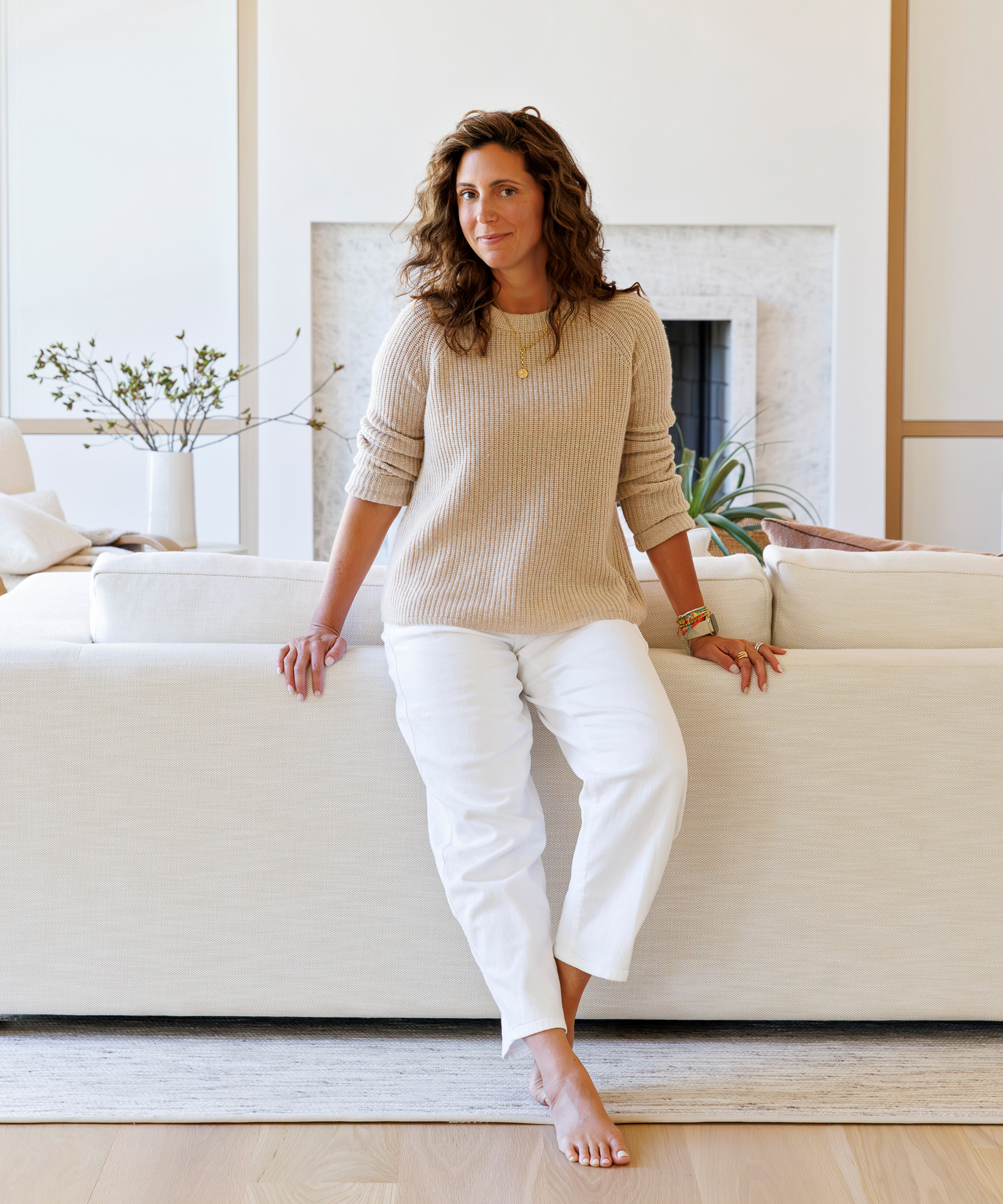 a portrait of susana standing in the living room with ivory jeans and an oatmeal sweater