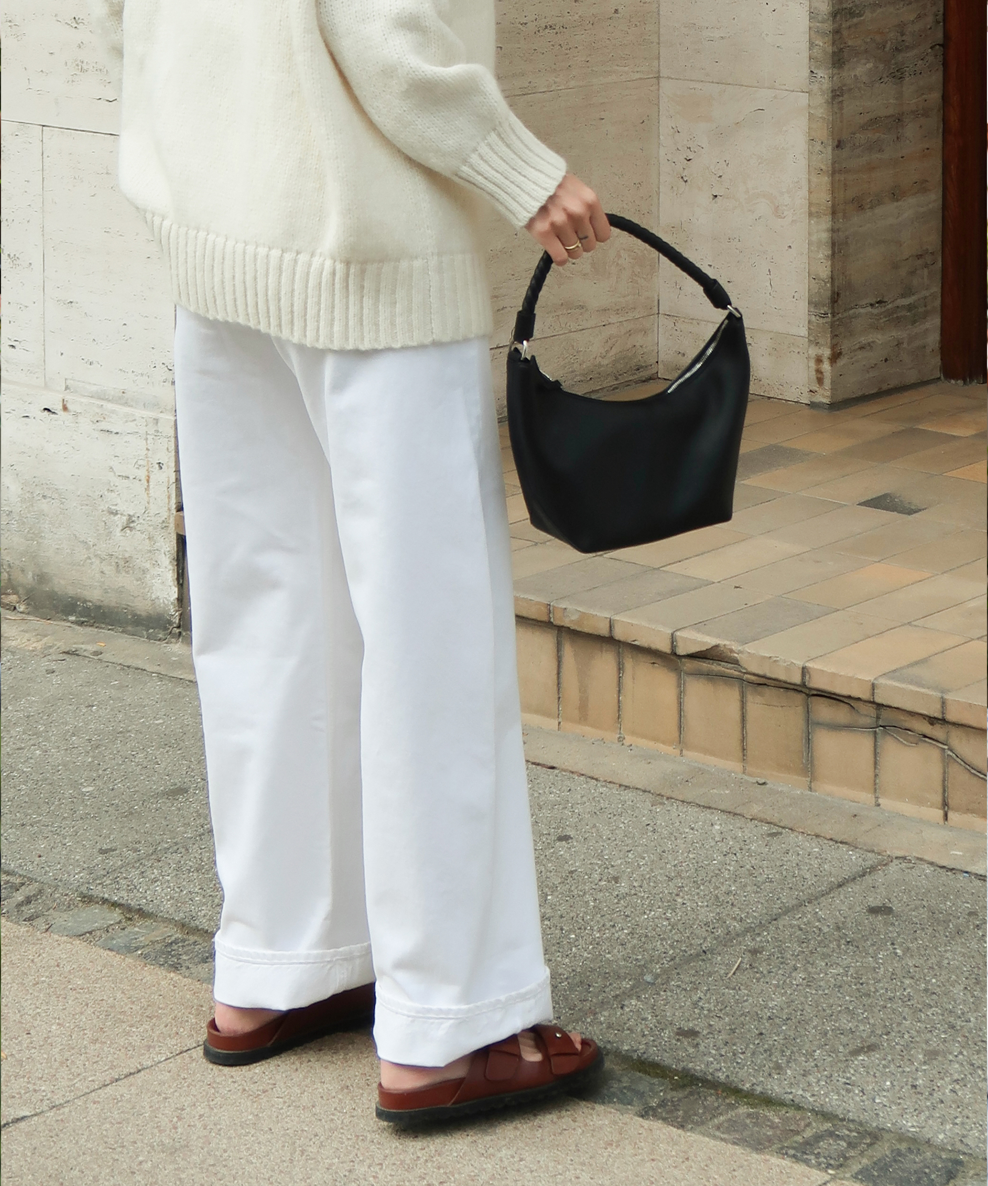 a woman in an ivory sweater and white pants with a black crescent bag standing on steps outside