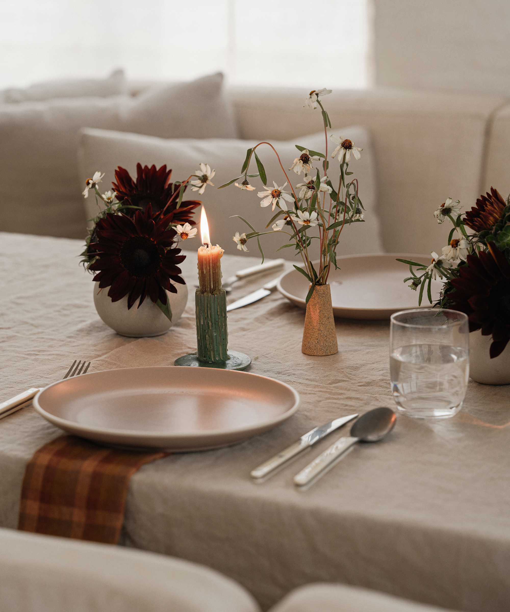 a candle lit next to a ceramic plate on a taupe tablecloth with simple fall florals