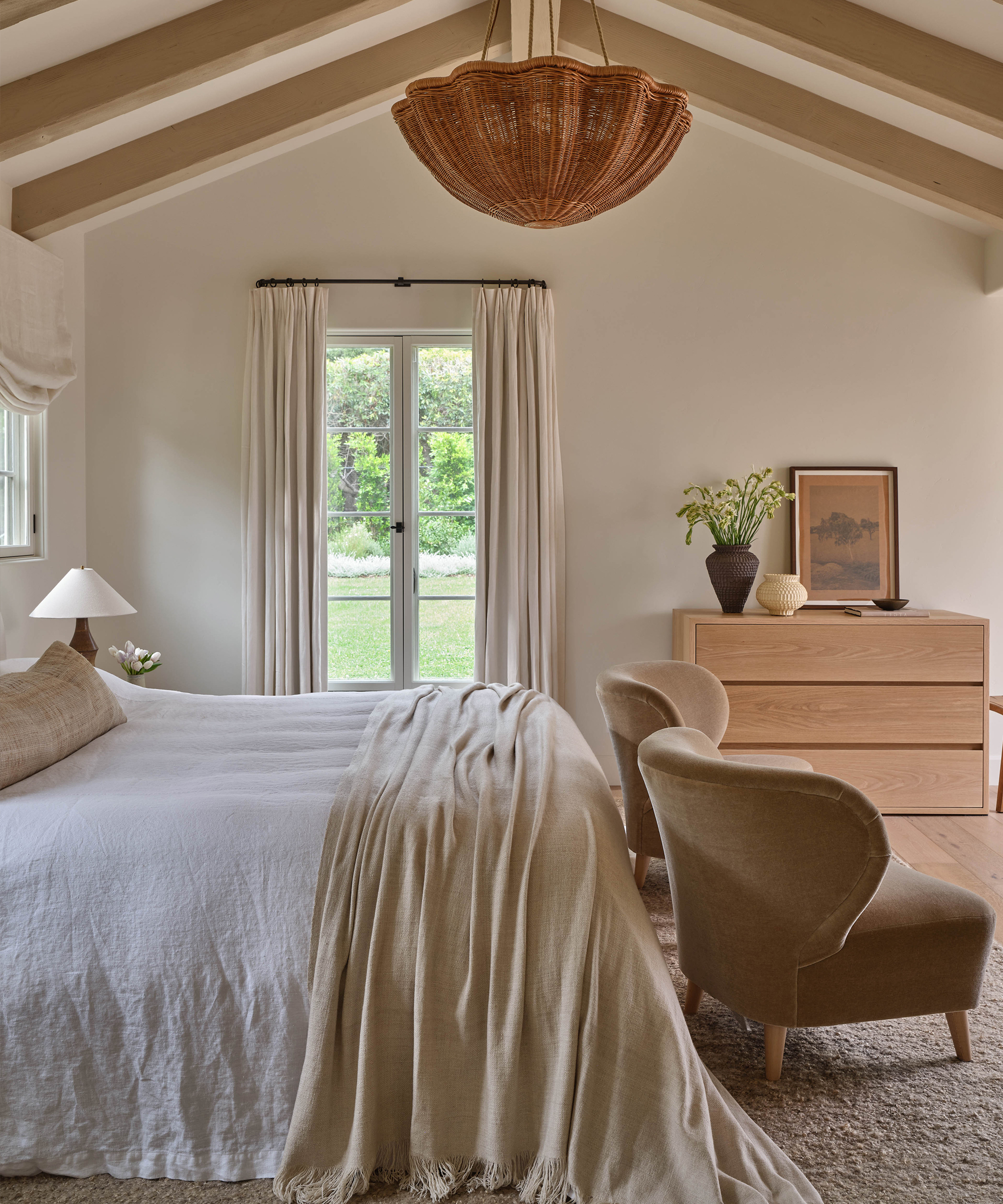 a primary bedroom with vaulted ceilings and two velvet accent chairs in front of a queen bed with linen bedding