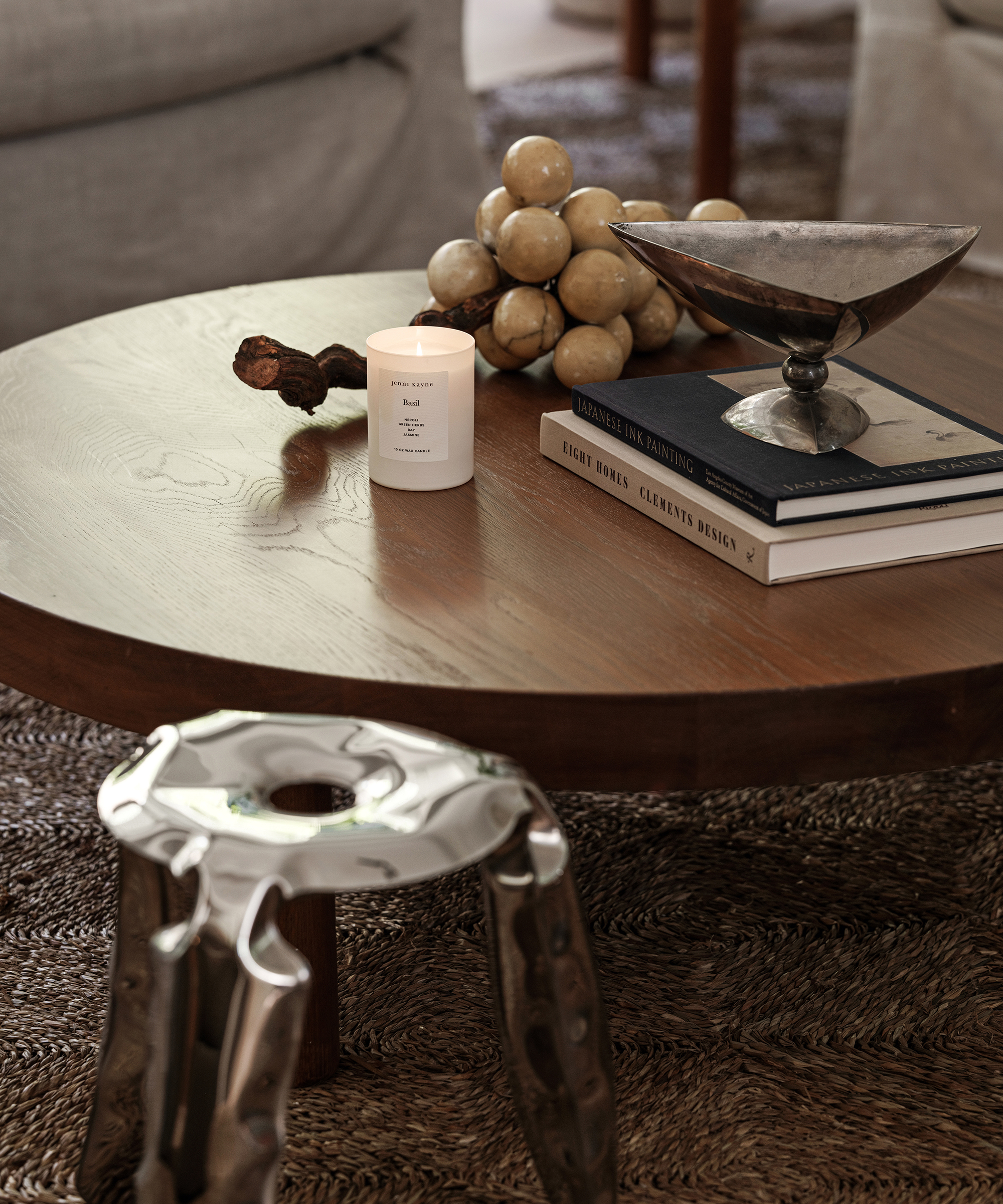 a dark wood coffee table with coffee table books and a burning candle and a silver stool