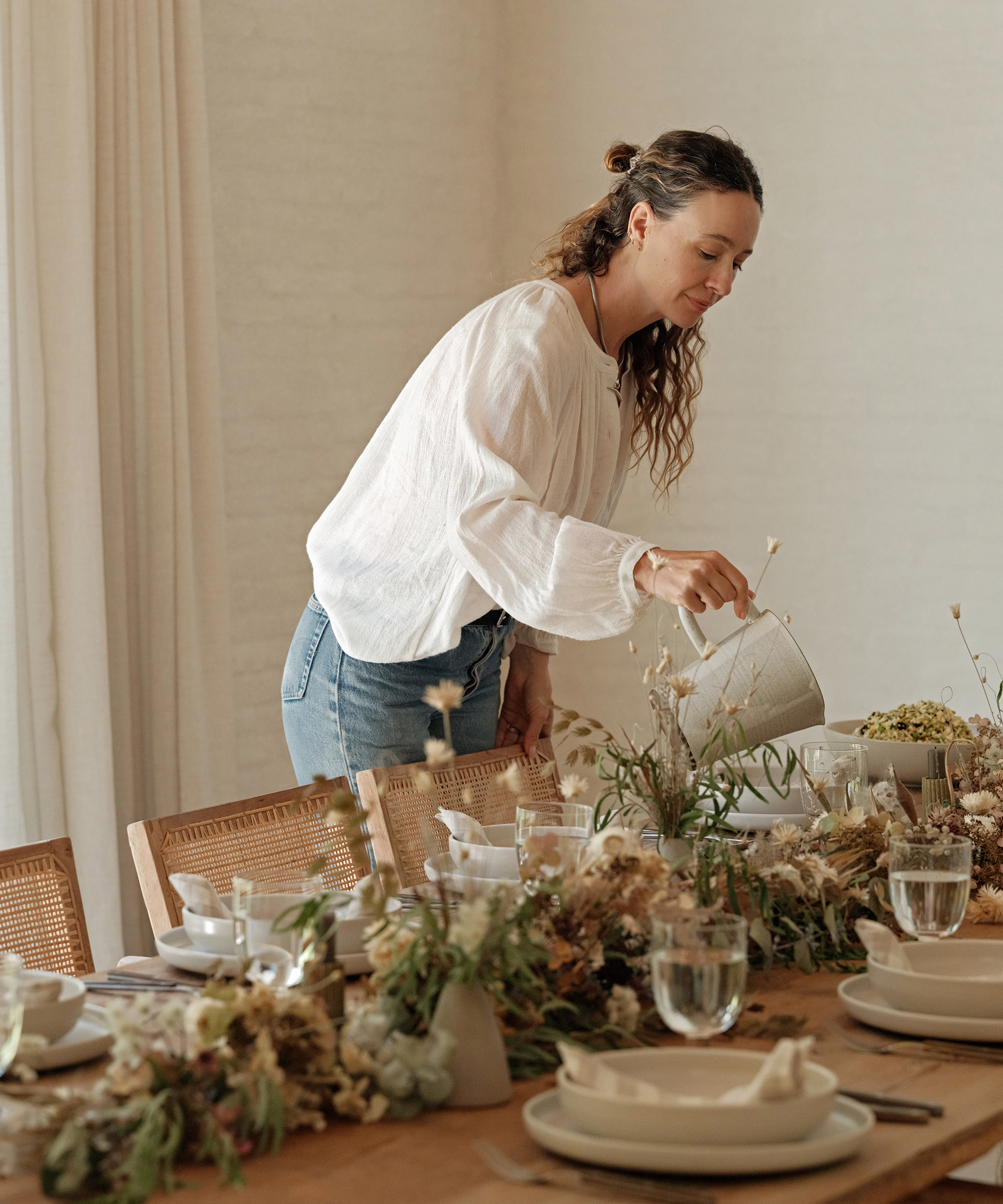 jenni pouring glasses of water on a table set with fall inspired florals and ivory tableware