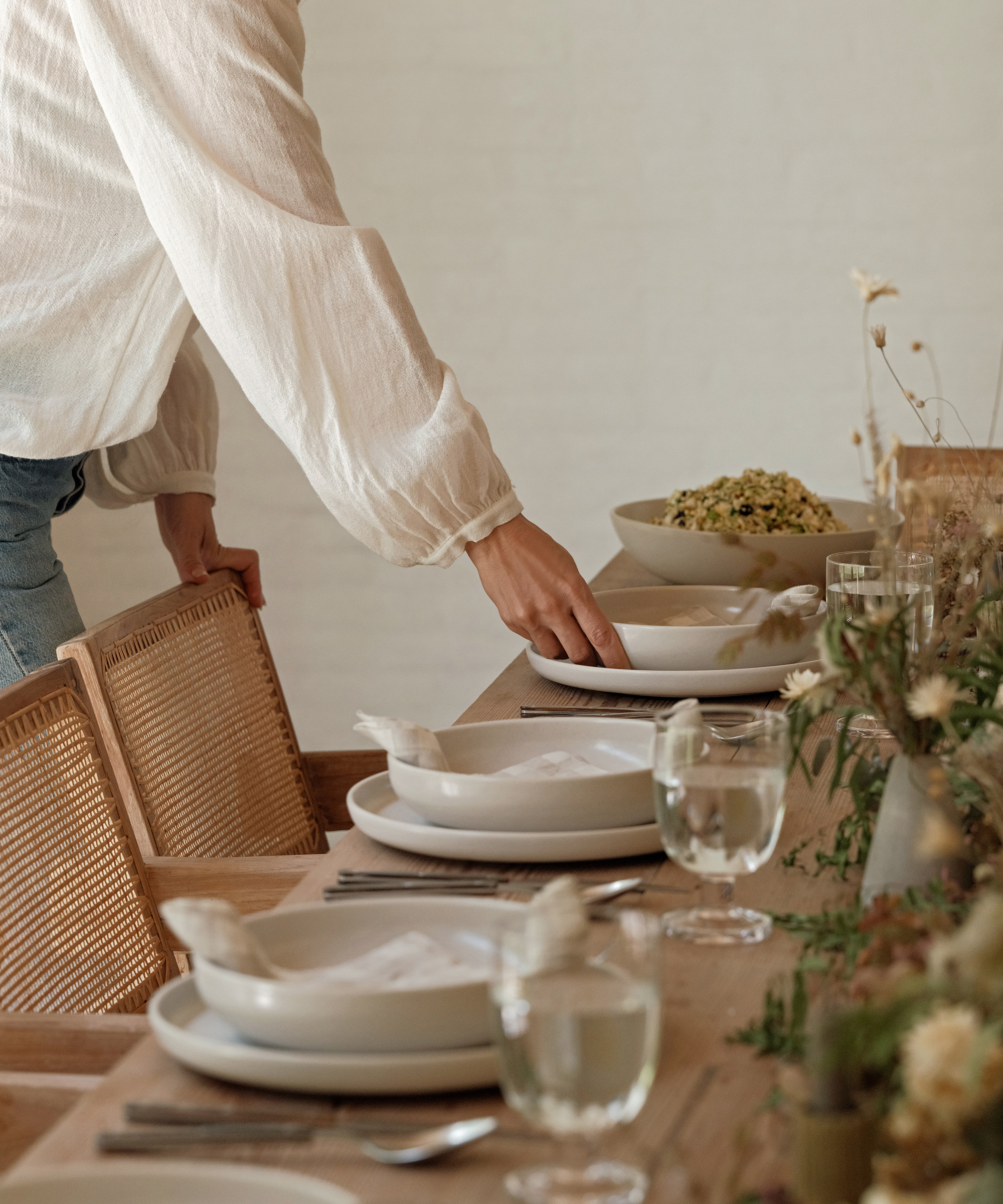 a person setting a table with ivory plates and gingham napkins and clear water glasses