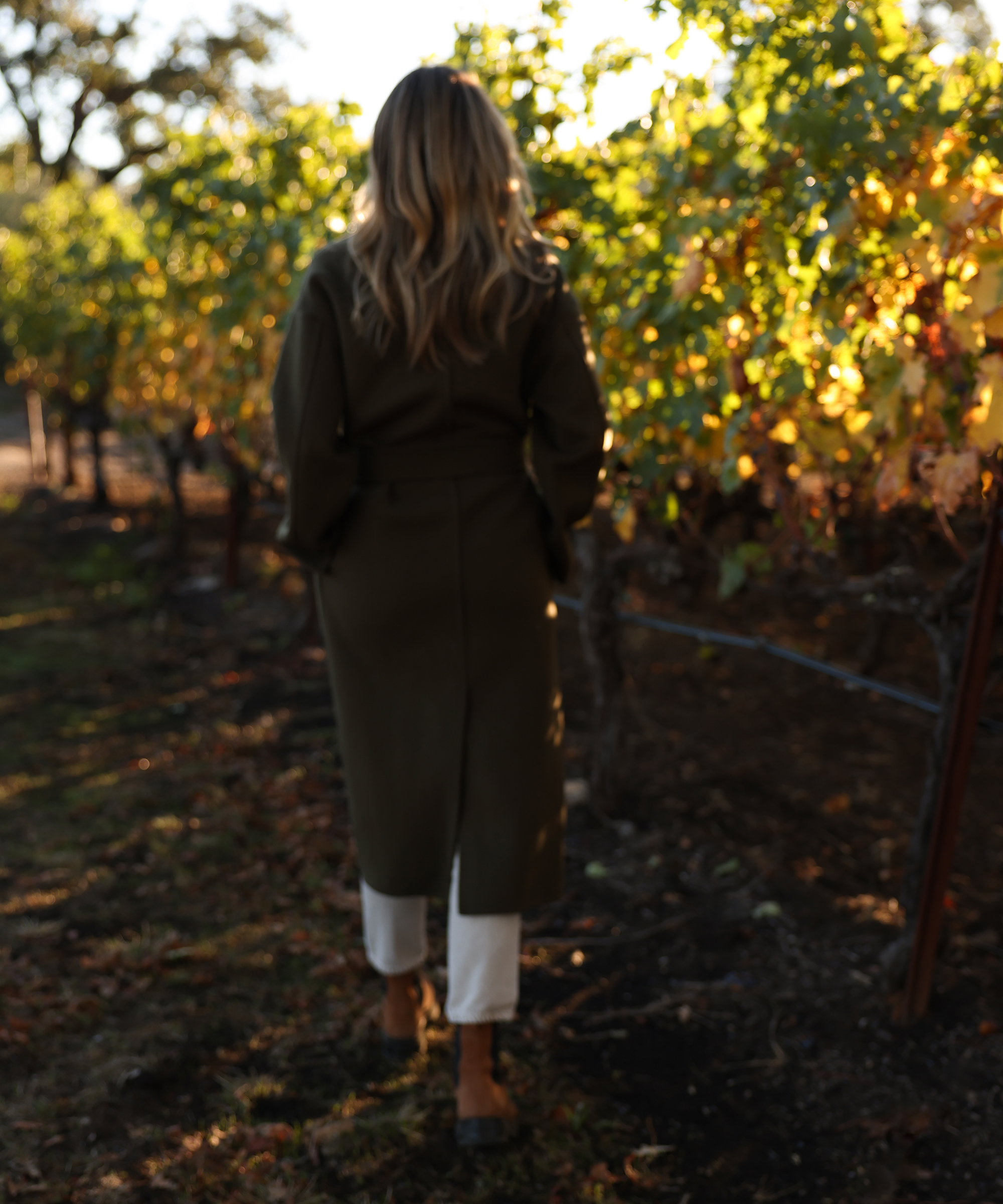 caitlin walking in a vineyard in an olive coat with boots on