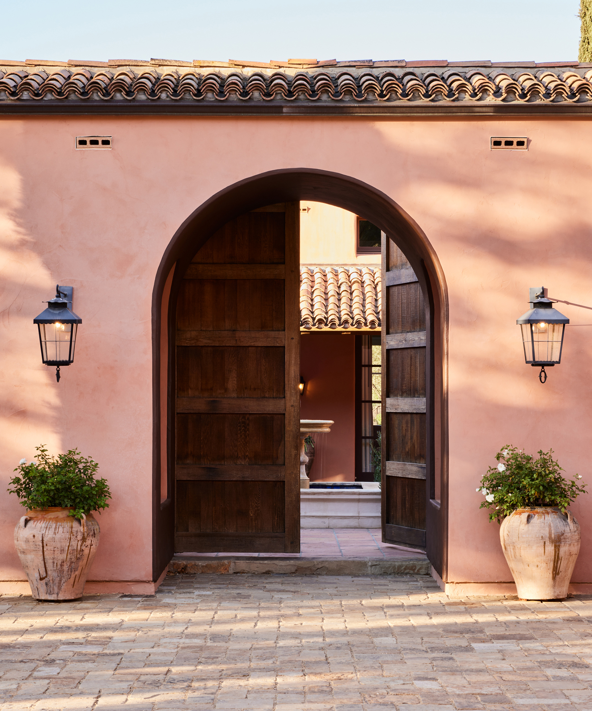 a pink stucco villa with a large wooden arched door with a stone driveway