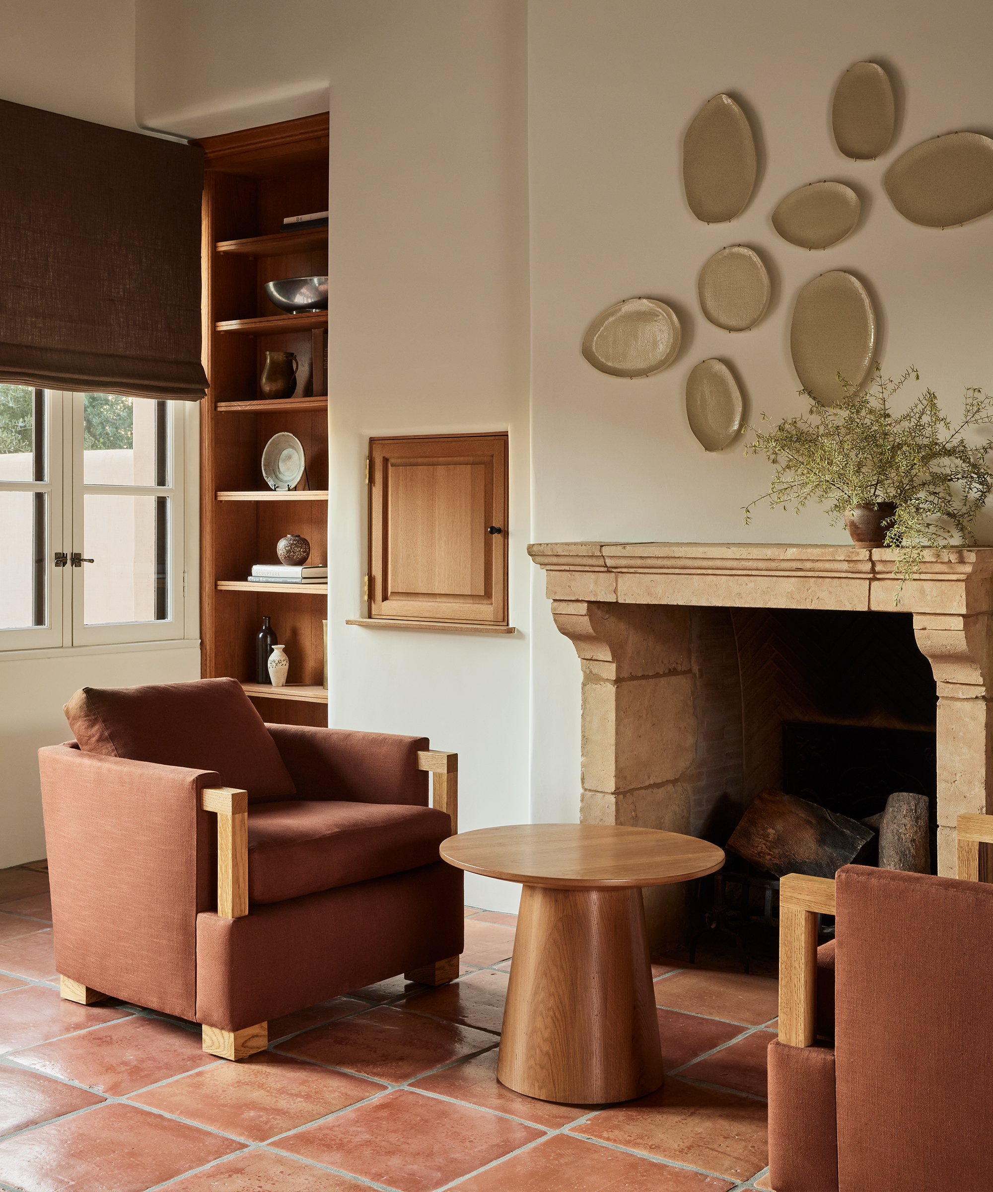 a brown accent chair on red clay tiled floors with a wood side table next to a stone fire mantle
