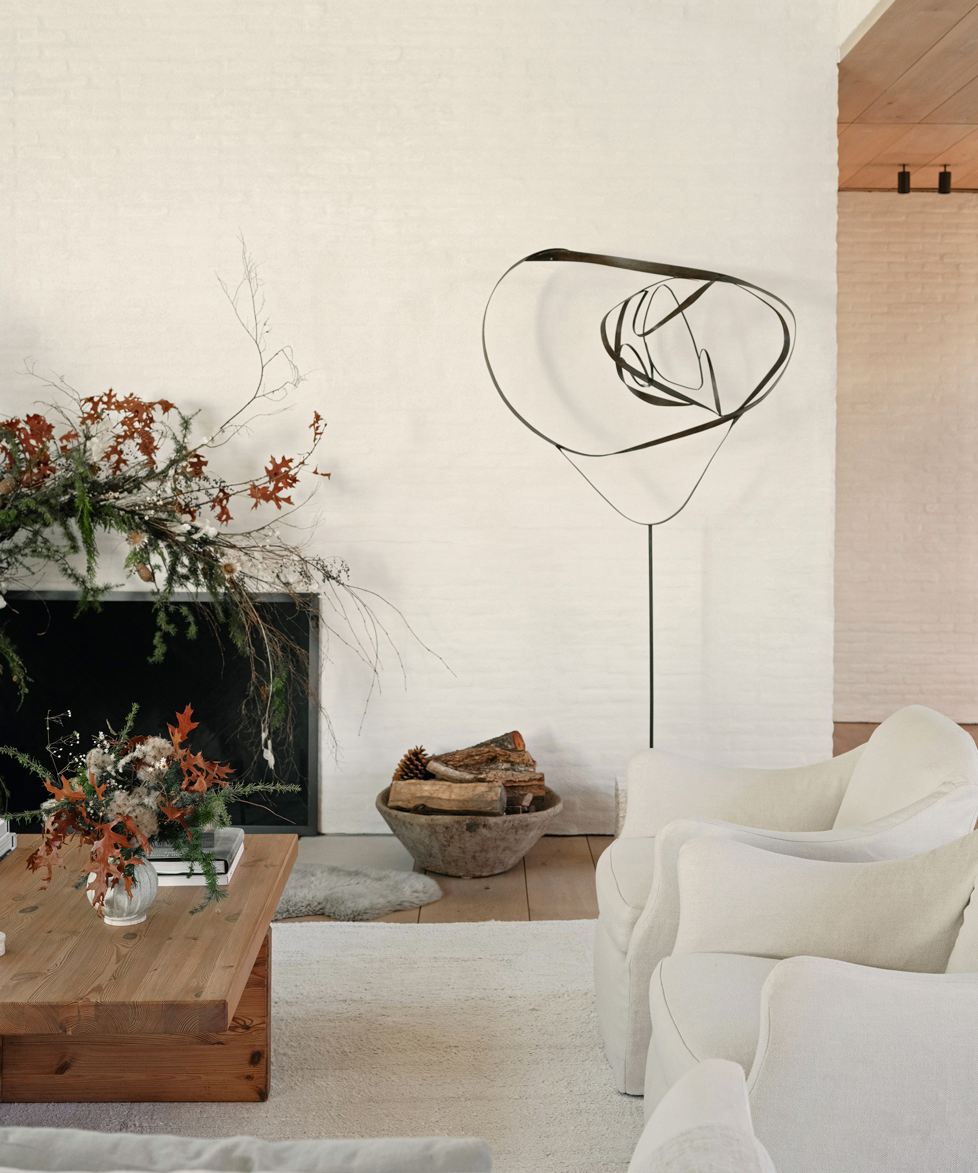a living room with an ivory brick wall, a large wooden coffee table and two taupe accent chairs with an ivory rug and a black iron sculpture