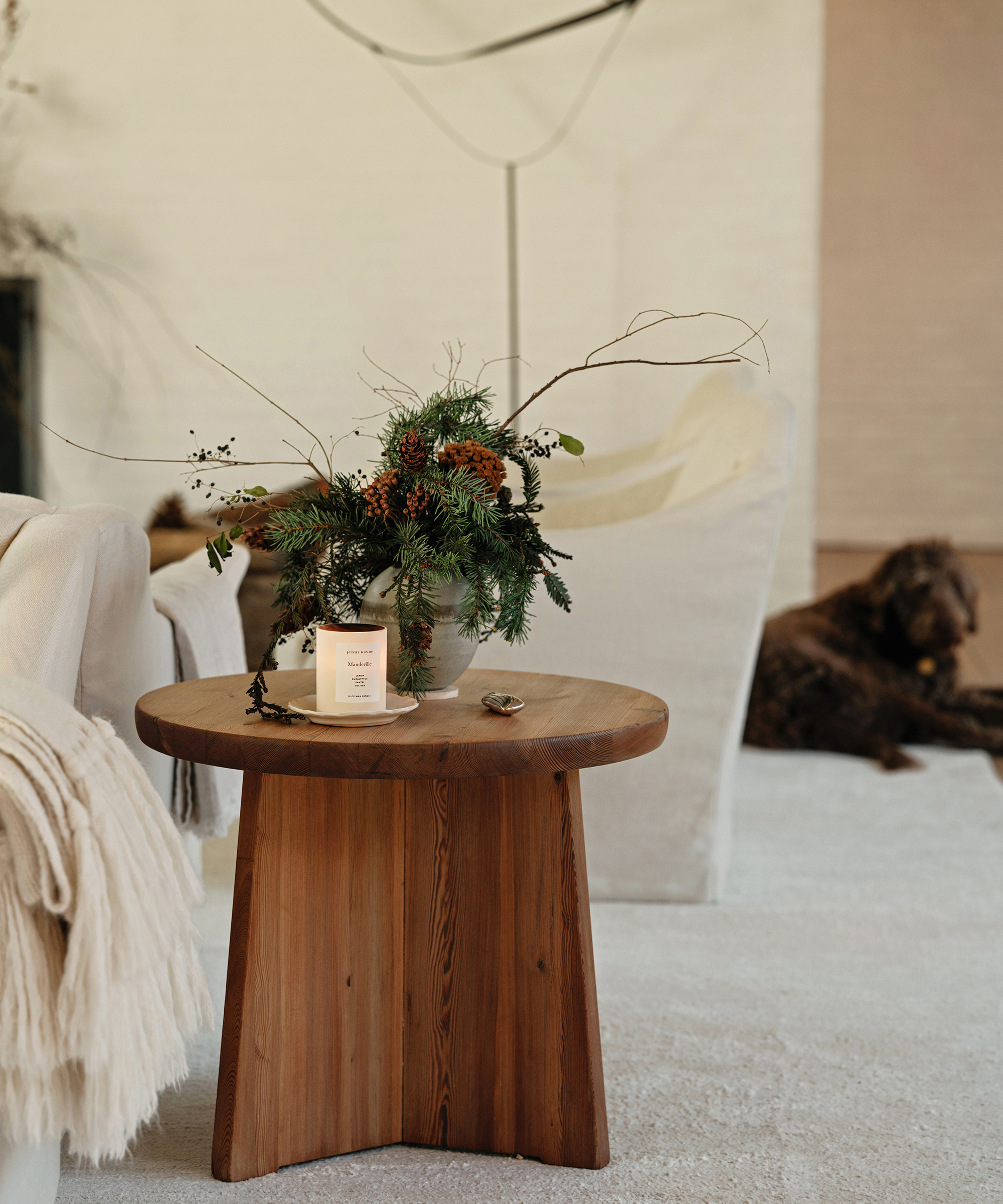 a wooden side table with a pine floral arrangment and a candle on an ivory rug