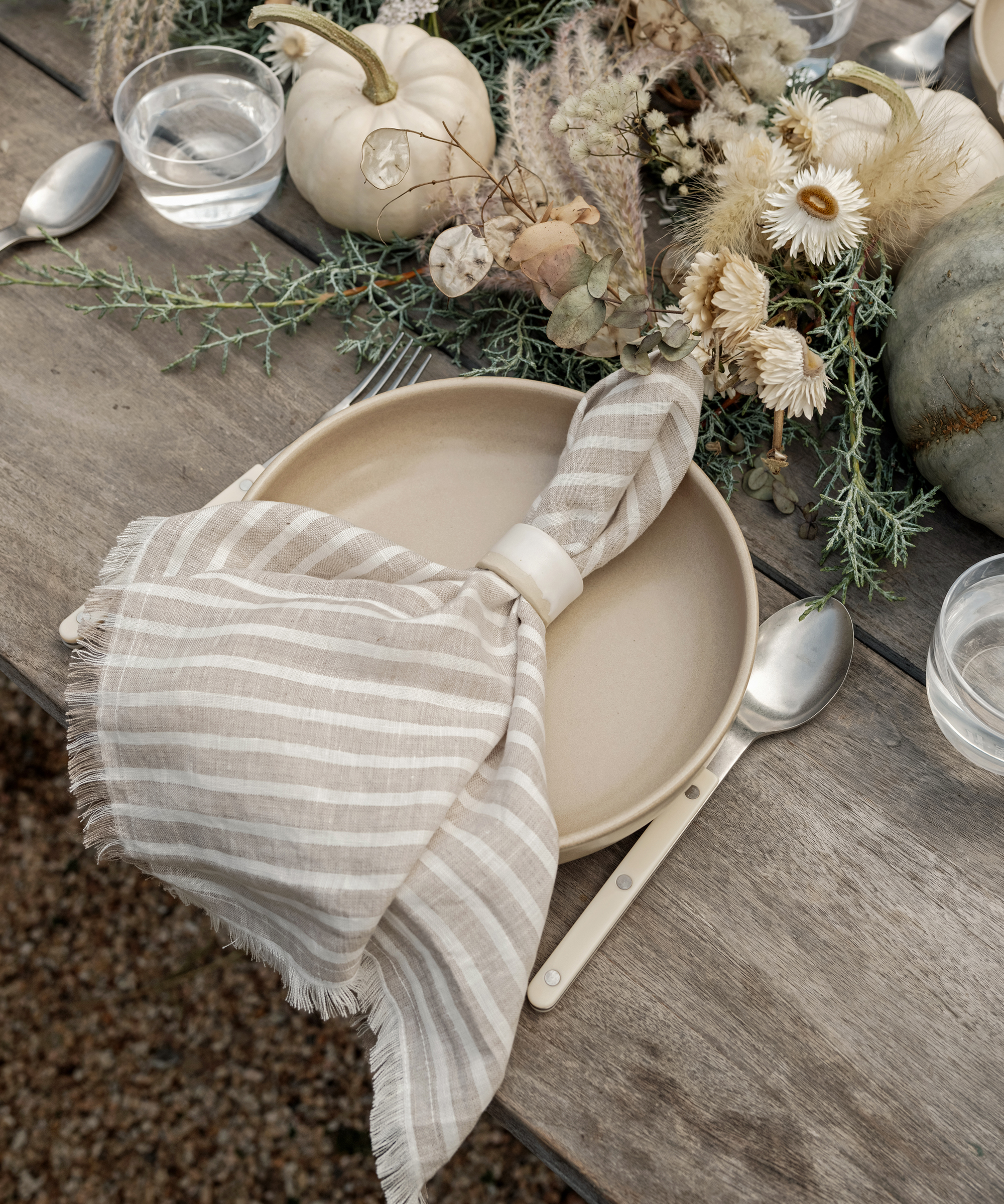 a place setting on an outdoor table with a linen striped napkin and a taupe bowl with ivory cutlery