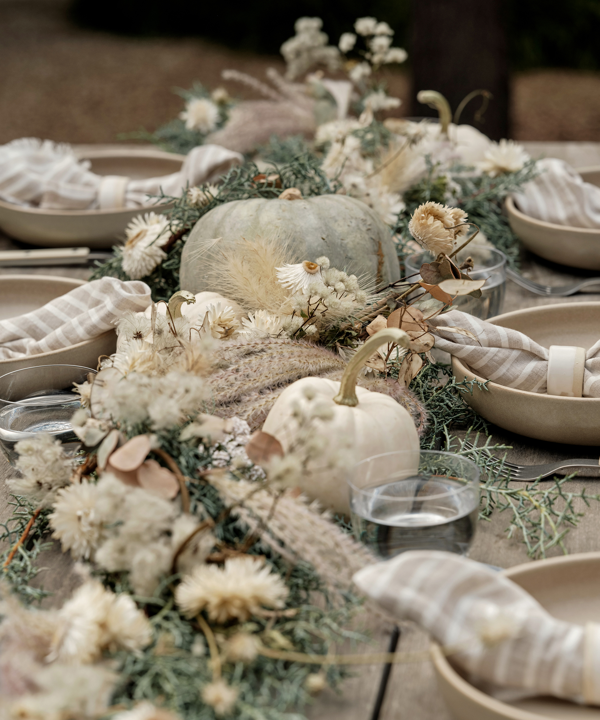 A rustic table set with neutral-toned plates, striped napkins, and clear glasses, decorated with white pumpkins and dried flowers evokes an autumn theme—perfect for showcasing treats from Sweet Laurel Bakery as a charming centerpiece.