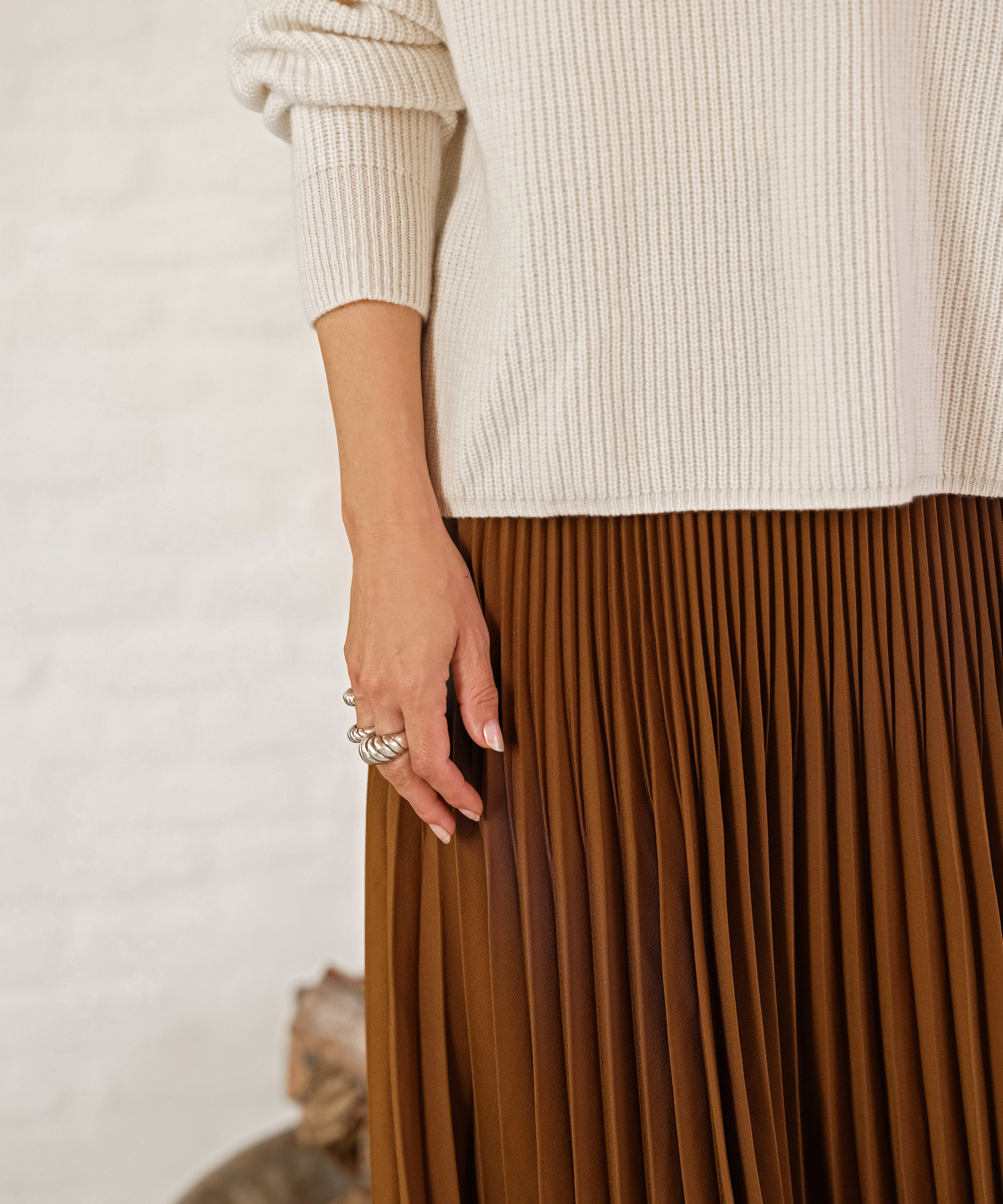 jenni wearing a crimson pleated skirt and an invory cashmere half zip in front of a white brick fireplace