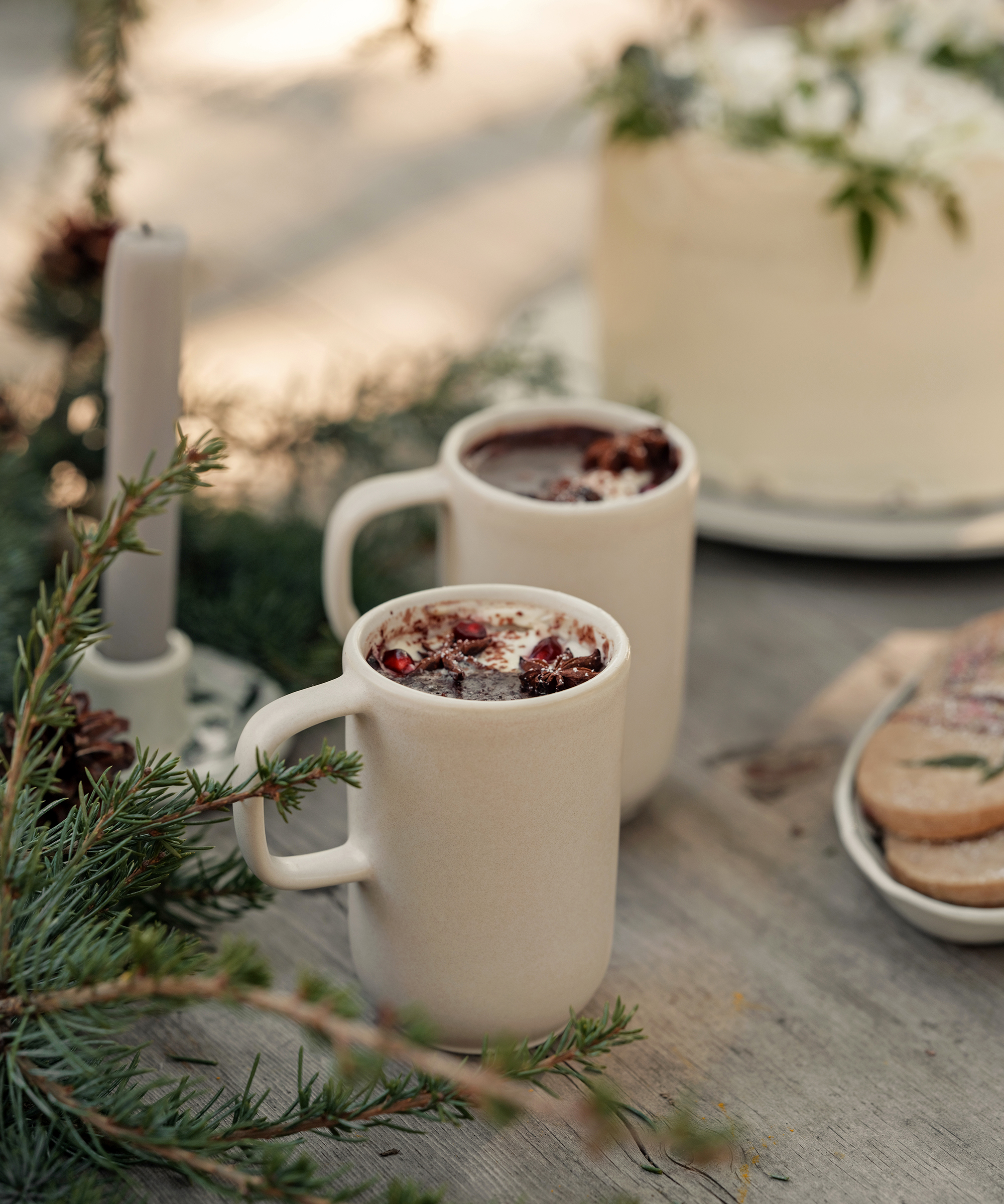 two taupe mugs of hot cocoa on an outdoor wood dining table