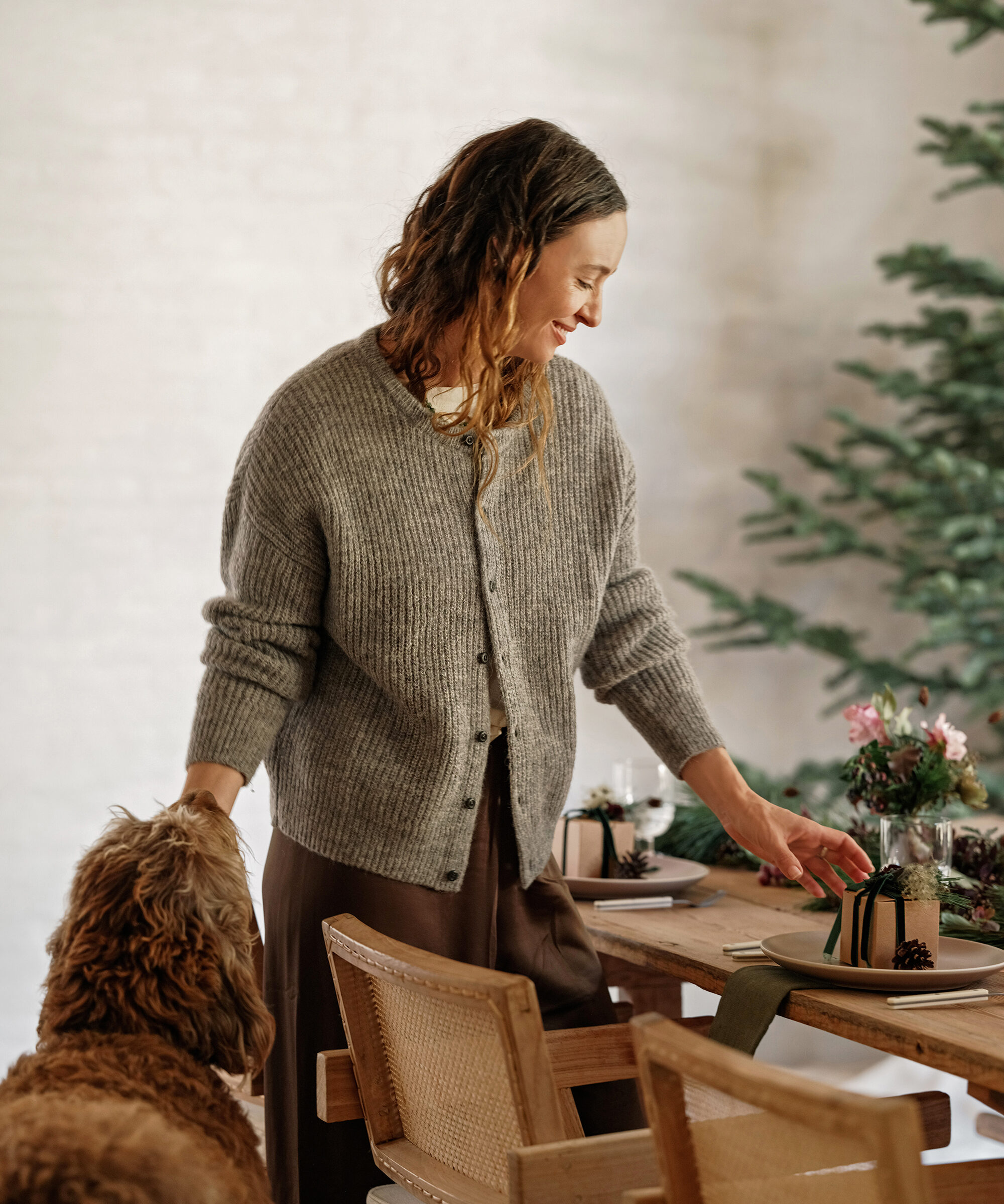 jenni in a grey sweater in her dining room petting her dog and fixing a plate on the table