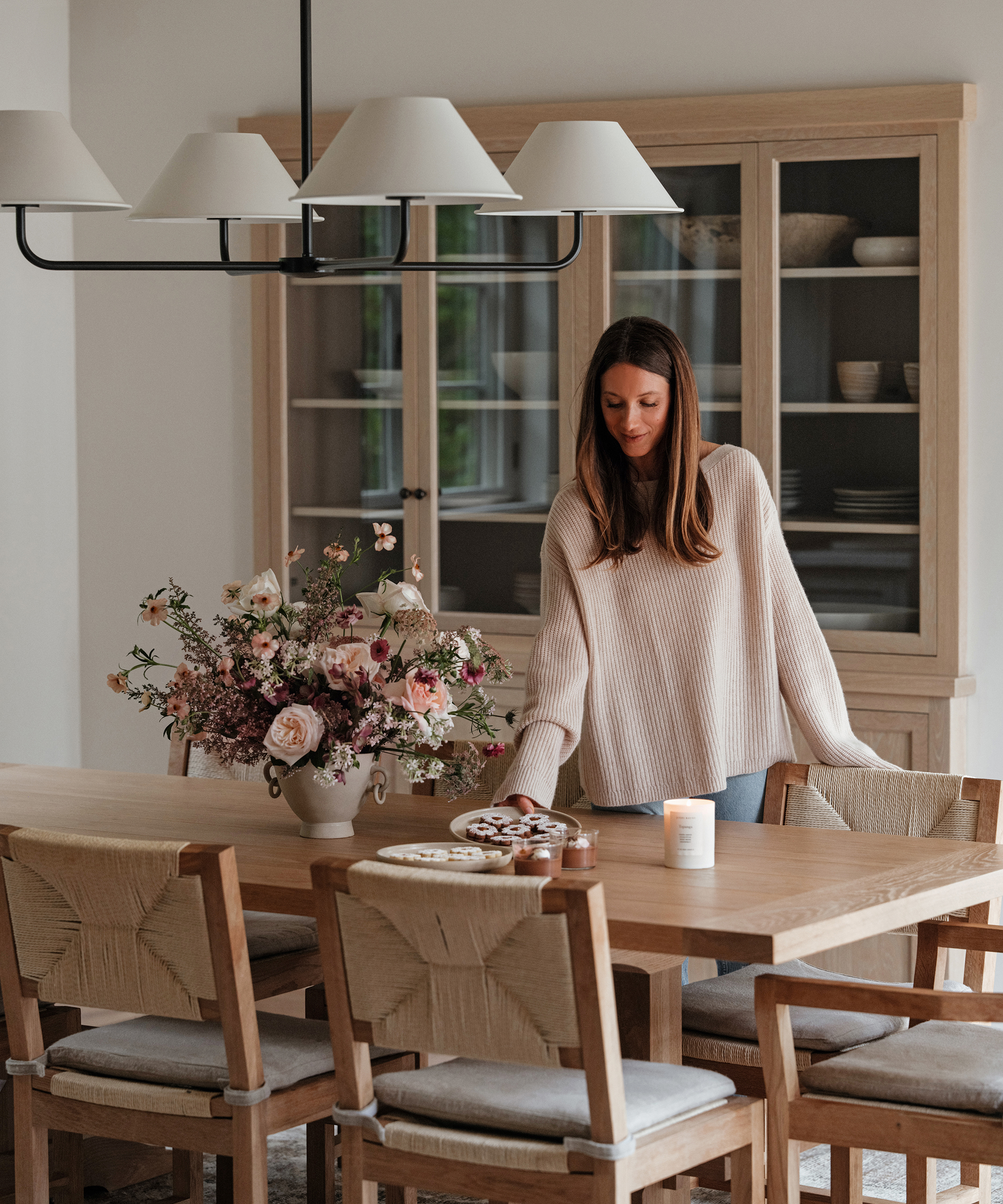 danielle adding a taupe plate of cookies to a wooden dining table with wooden dining chairs