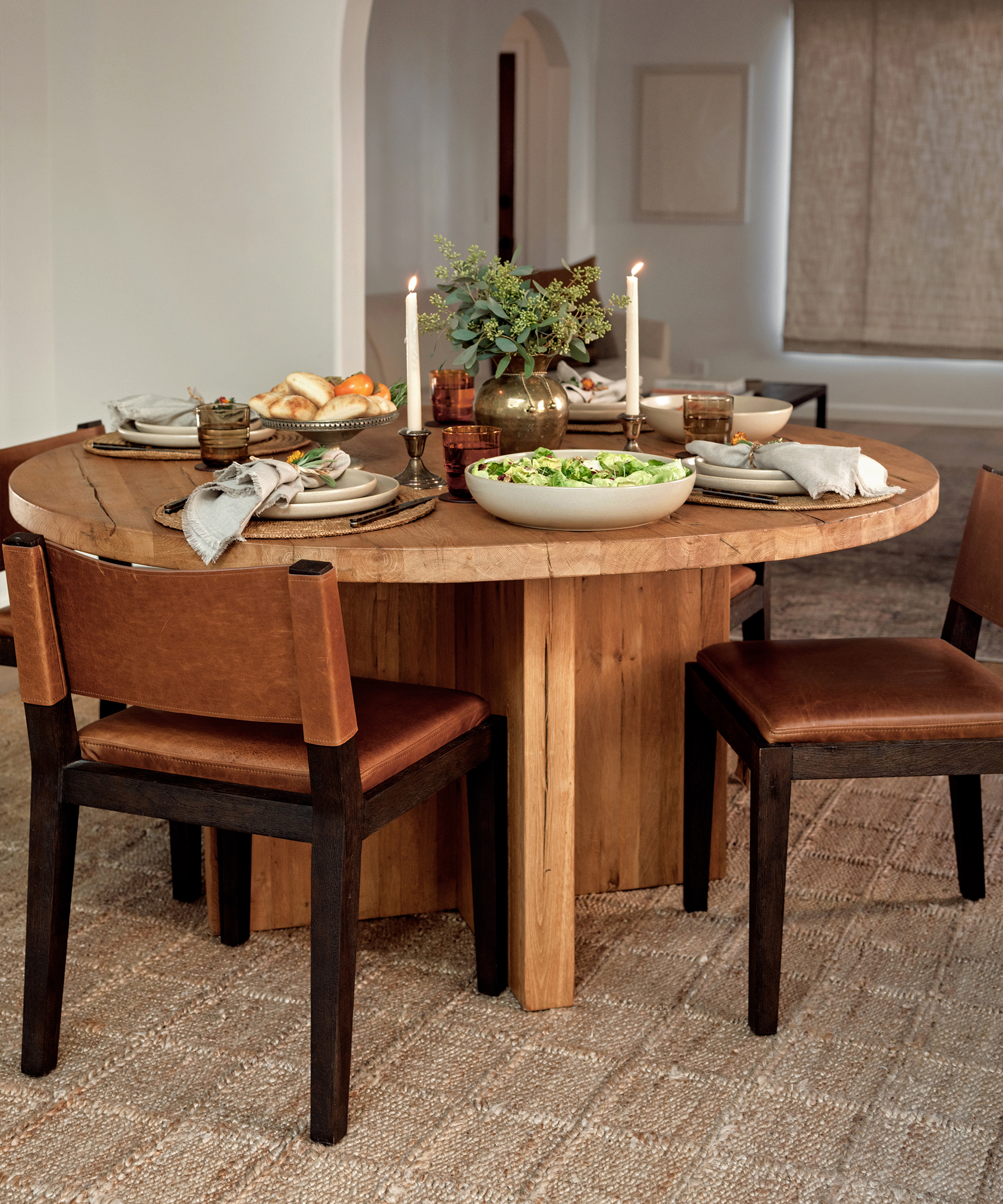a round wood dining table with leather dining chairs and food placed atop