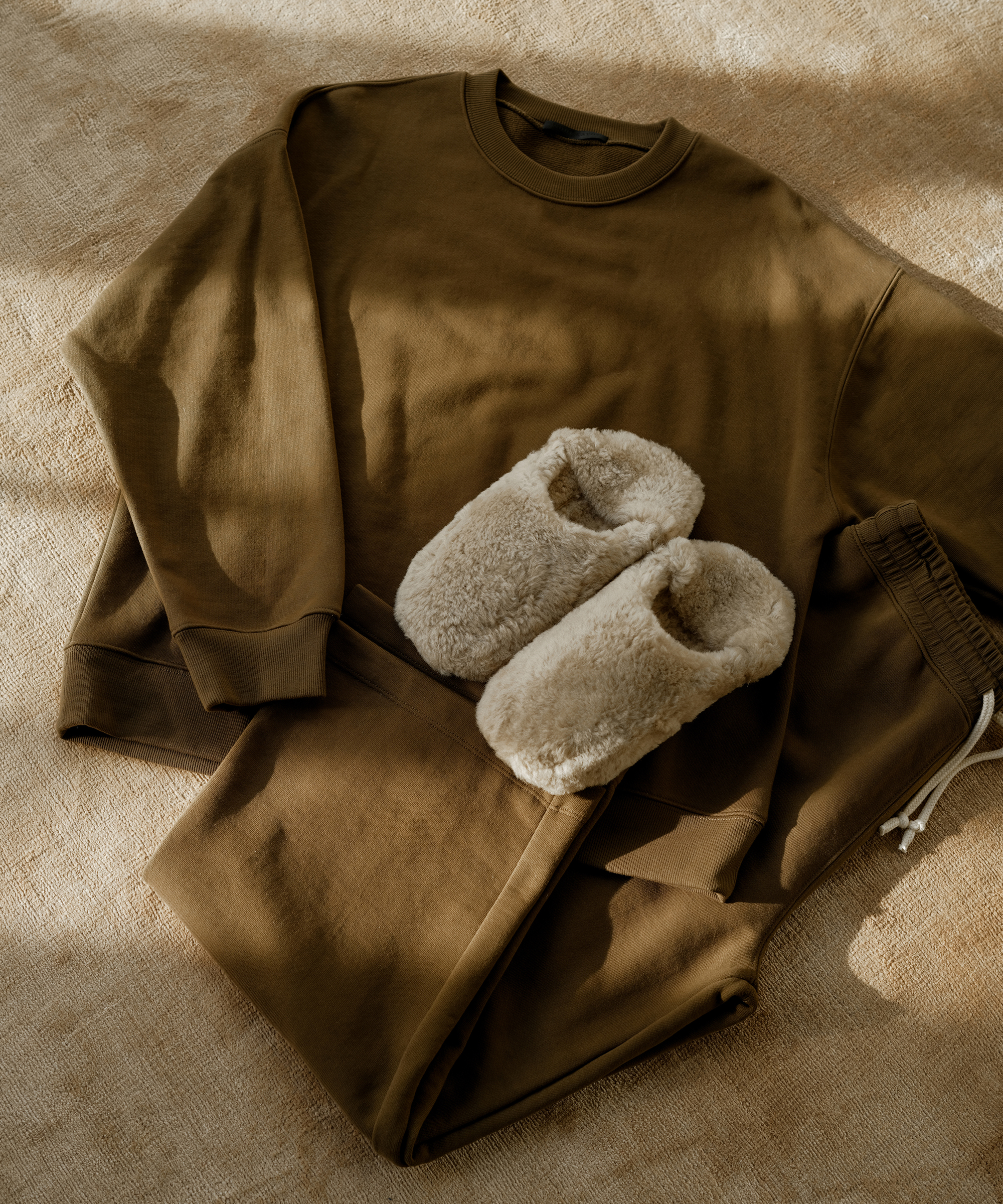 marina sweatershit and marina sweatpants in army green with ivory sherpa slippers on a plush area rug