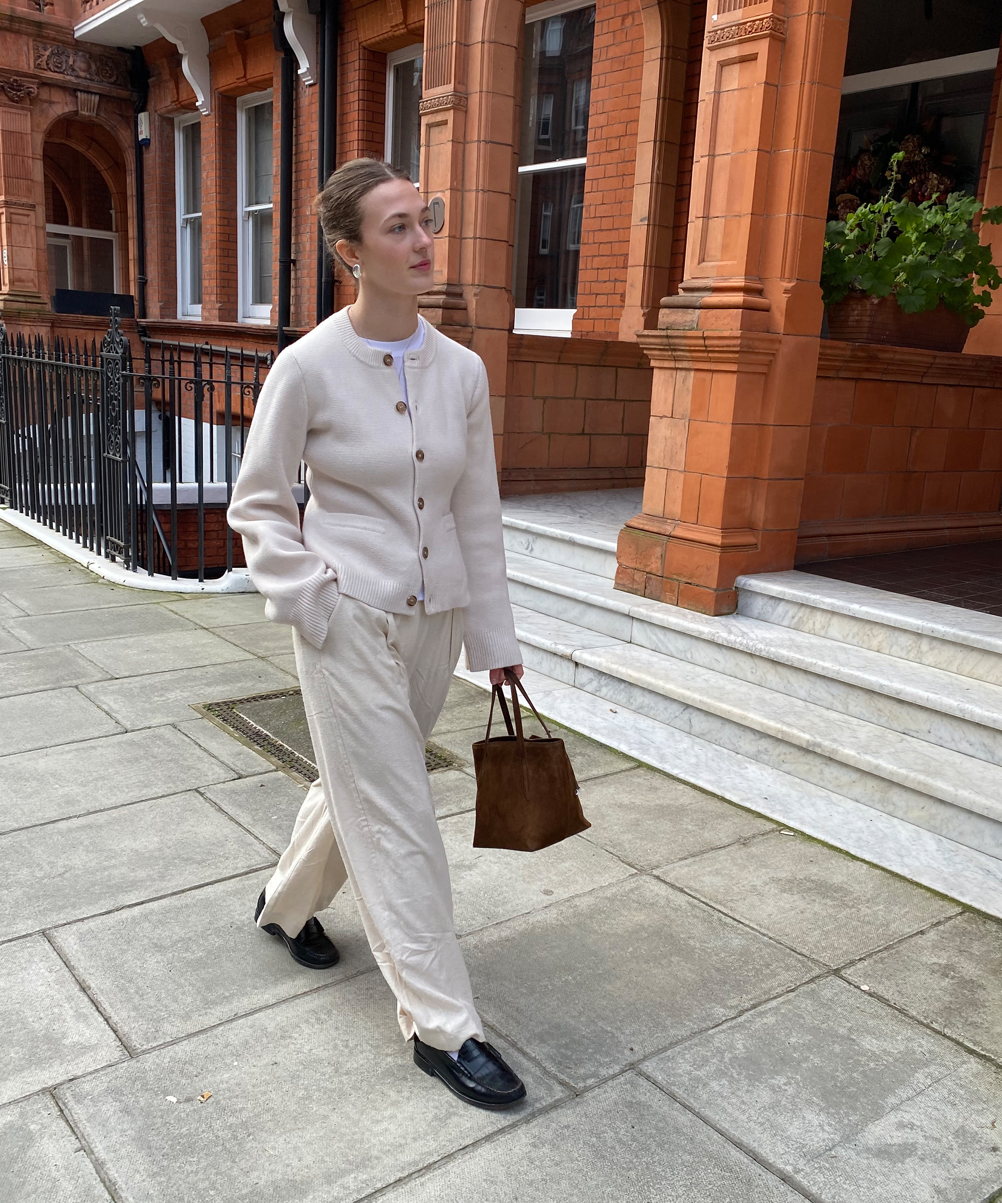 olivia in ivory relaxed trousers and an ivory cooper cardigan with black loafers walking down the street