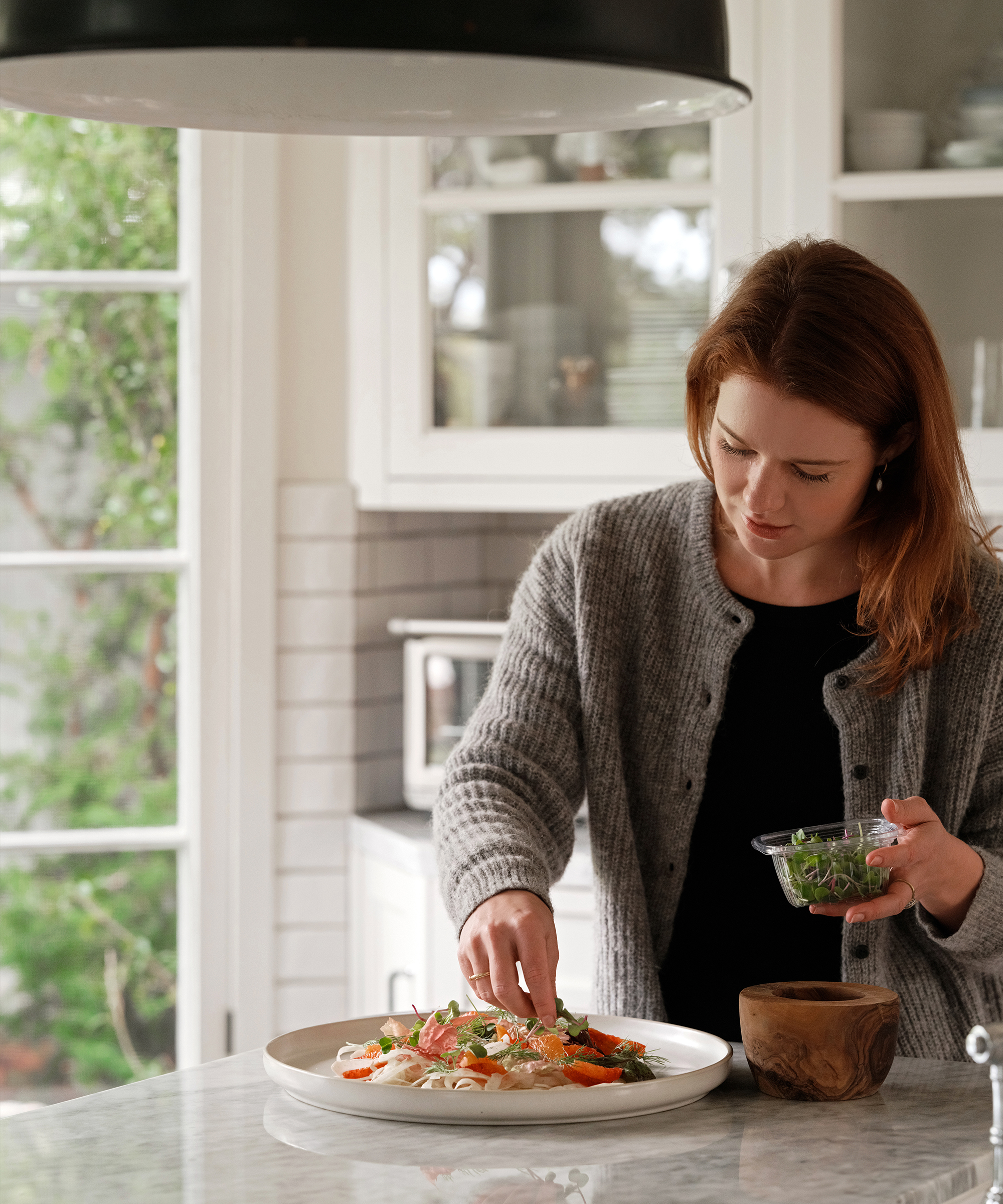 melissa placing garnish on a fennel and citrus salad in a white kitchen white marble countertops