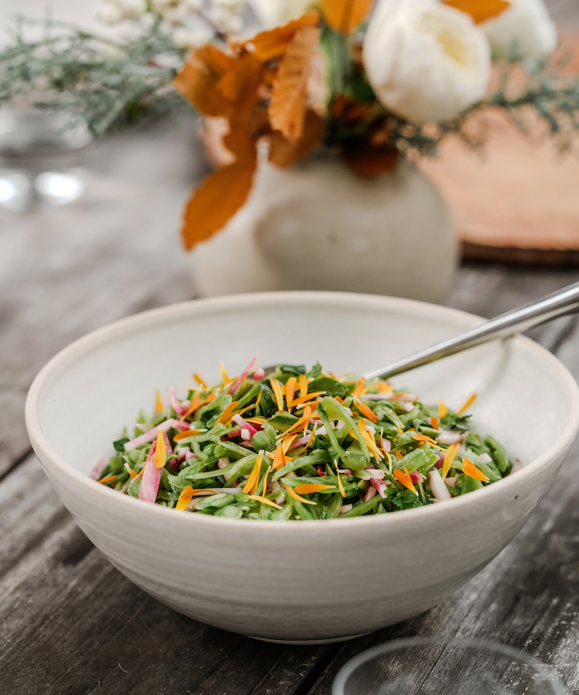 an ivory serving bowl with a snap pea salad on an outdoor dining table