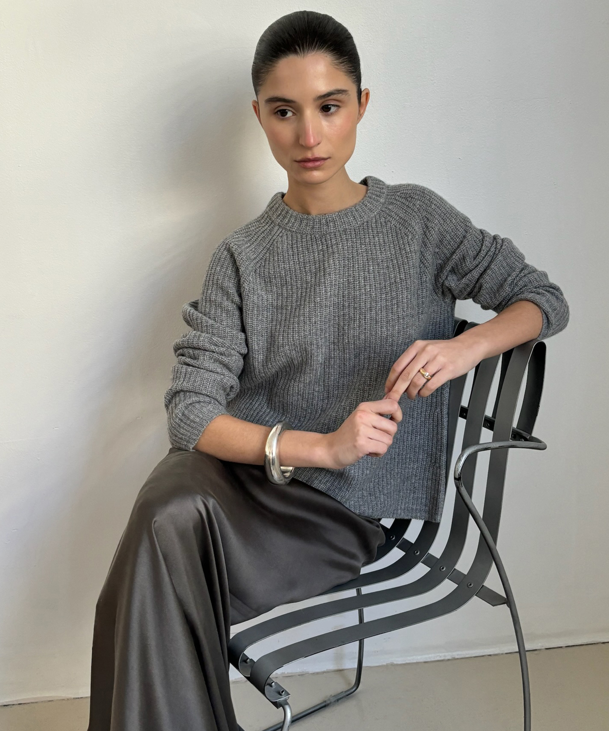 andrea sitting on a metal chair in a grey cashmere fisherman and grey silk skirt