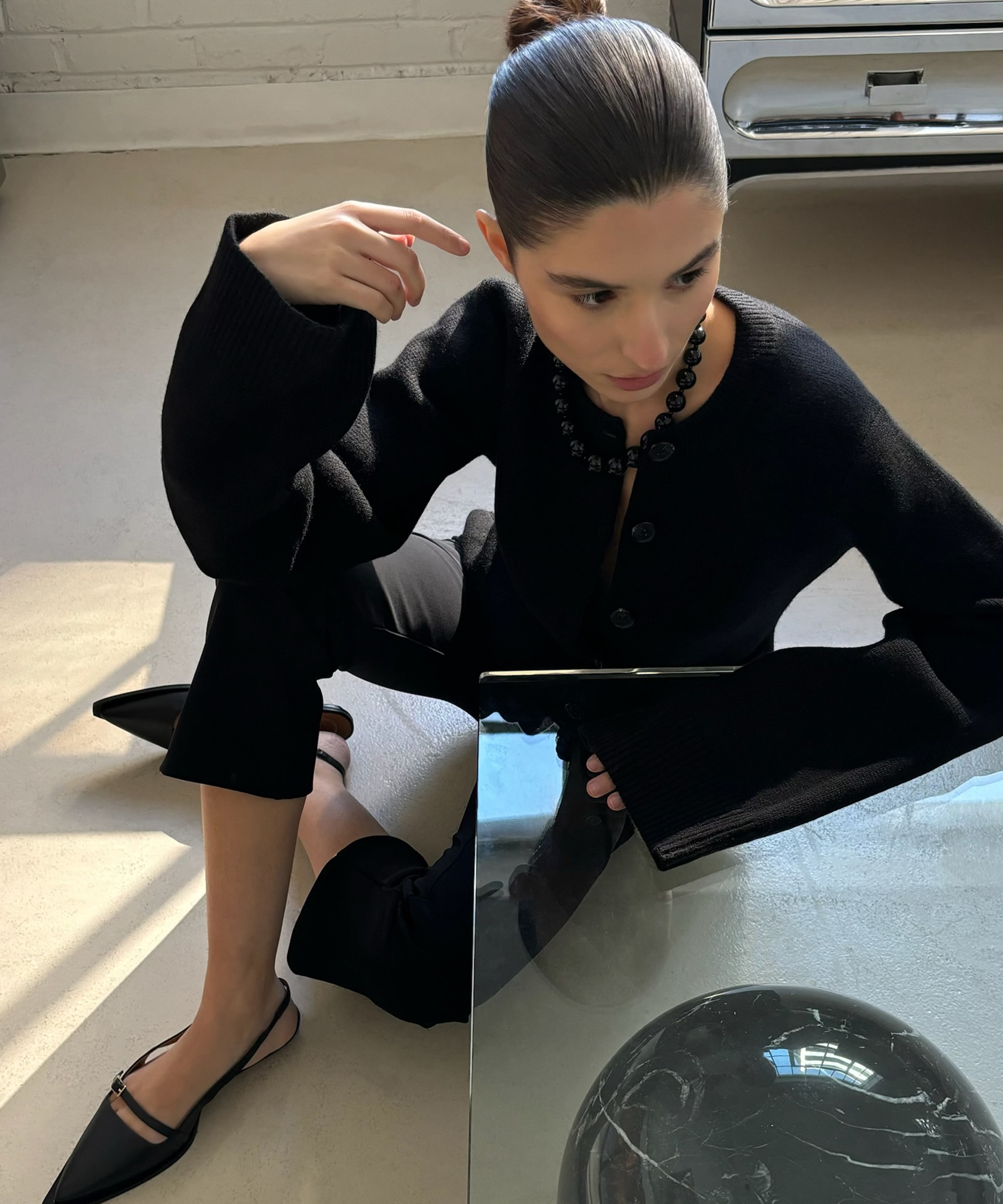 andrea sitting on the floor with her legs crossed resting against a coffee table in a black sweater and capris