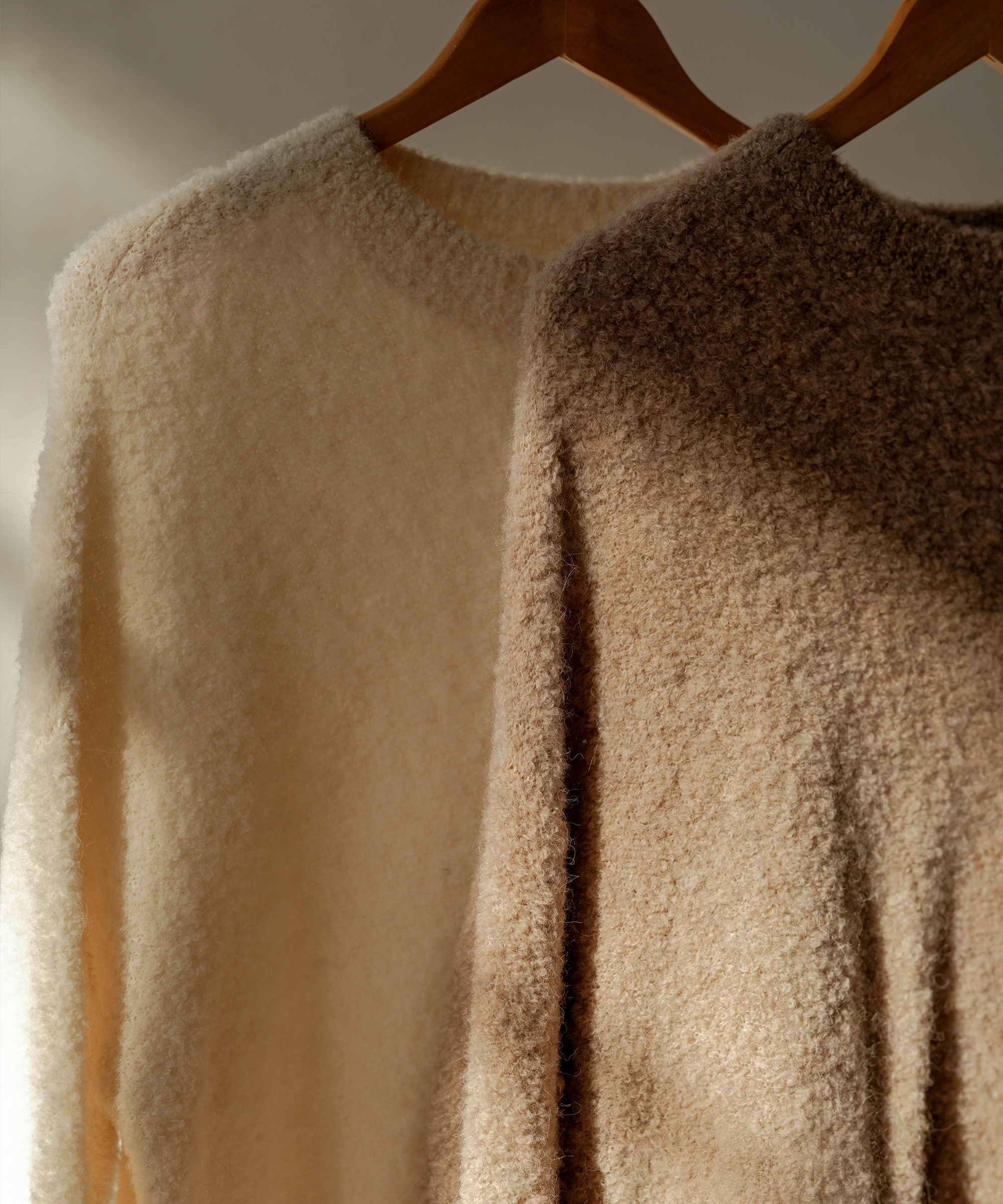 two hanging boucle crewneck sweaters in ivory and chestnut