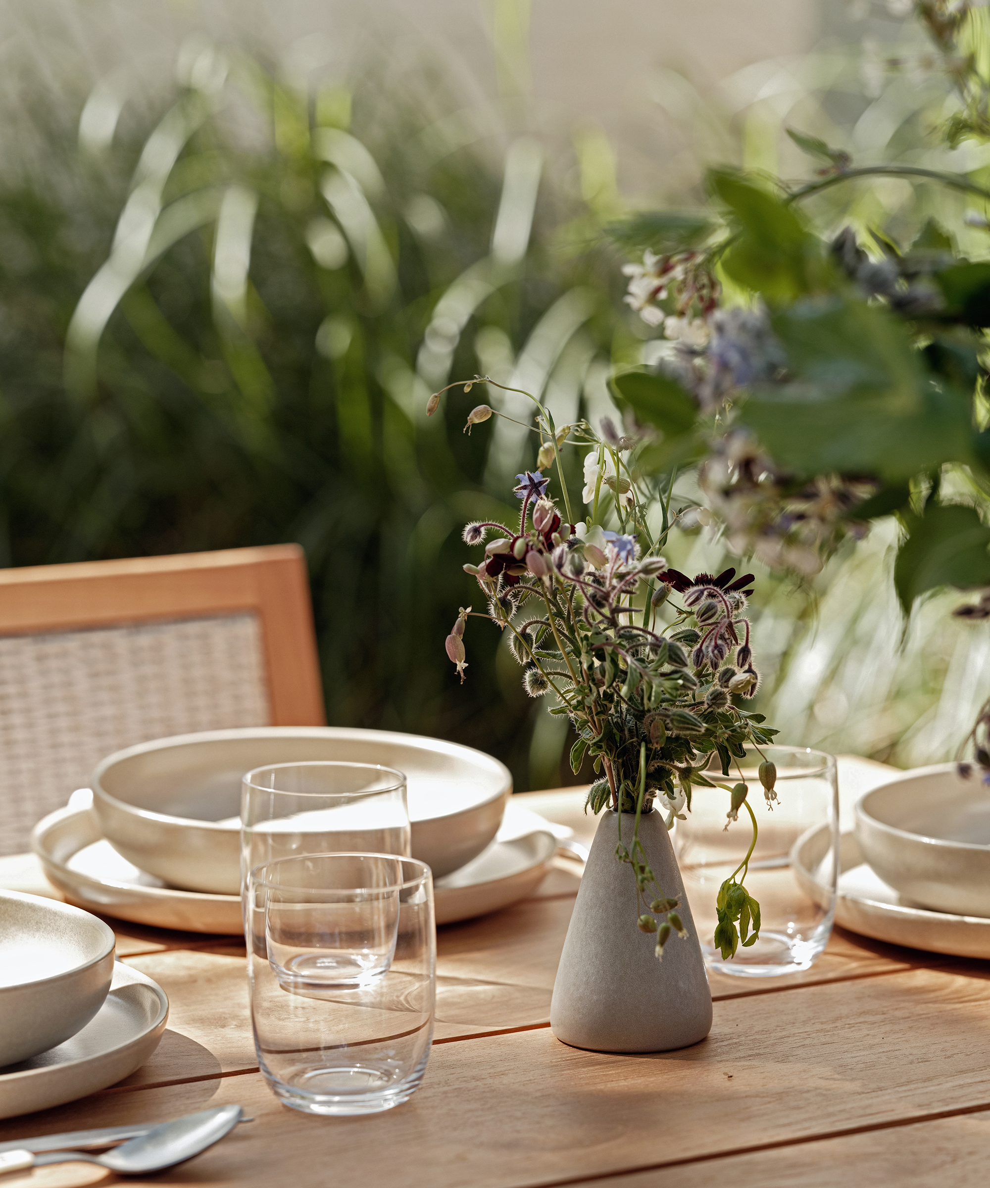 outdoor dining table with clear glasses and taupe dinner plates with a small vase of flowers