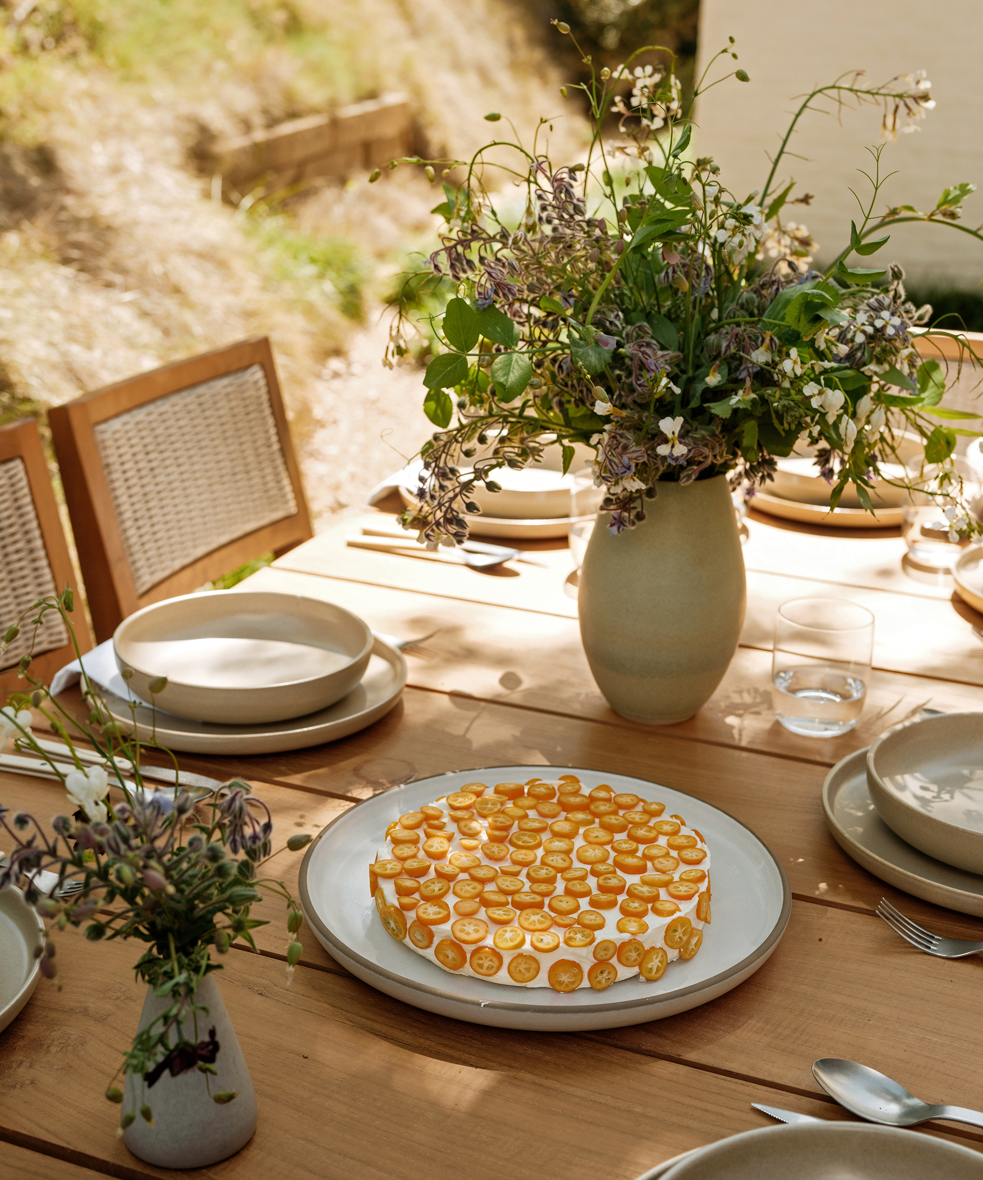 an outdoor dining table with taupe dinner plates and a large serving plate with a kumquat dessert