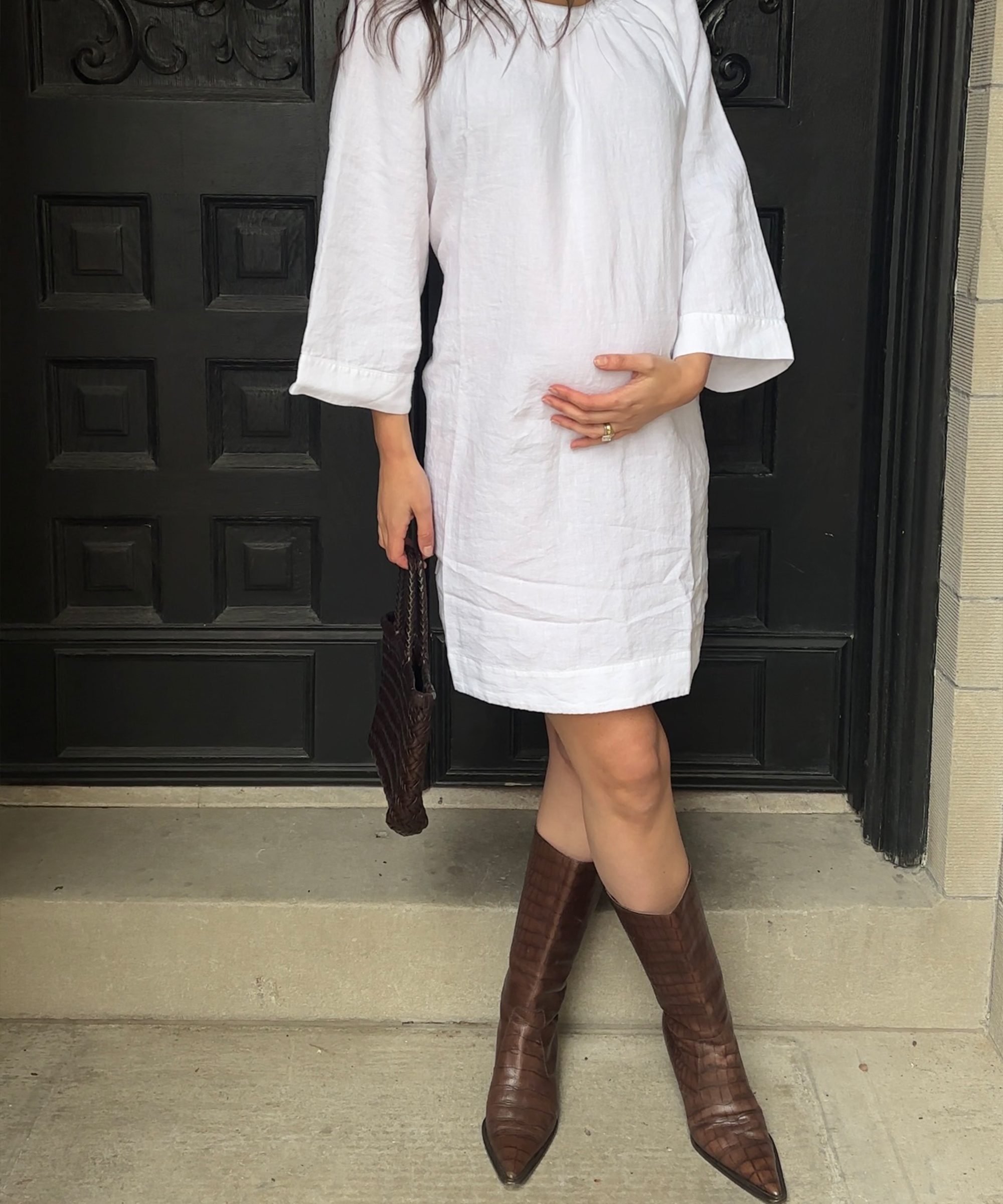 ilana standing in front of a black door wearing a white linen dress and brown boots