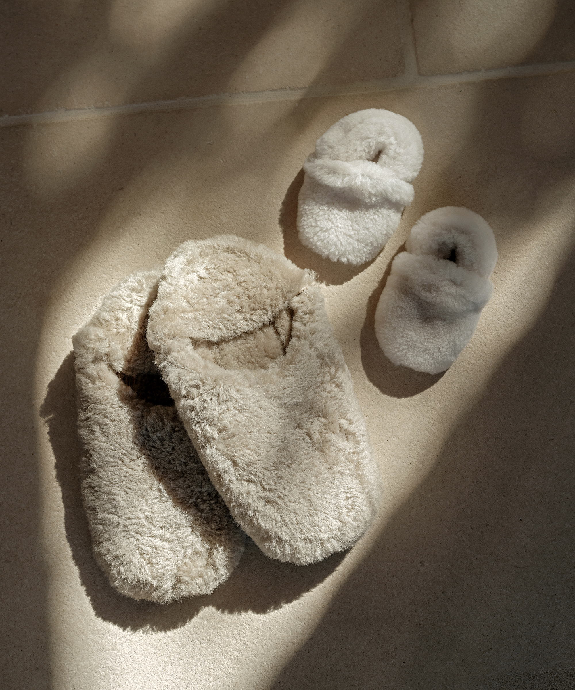 Two pairs of fluffy slippers, one large and one small, are placed side by side on a sunlit tiled floor, casting gentle shadows—a cozy scene perfect for celebrating Mother’s Day.