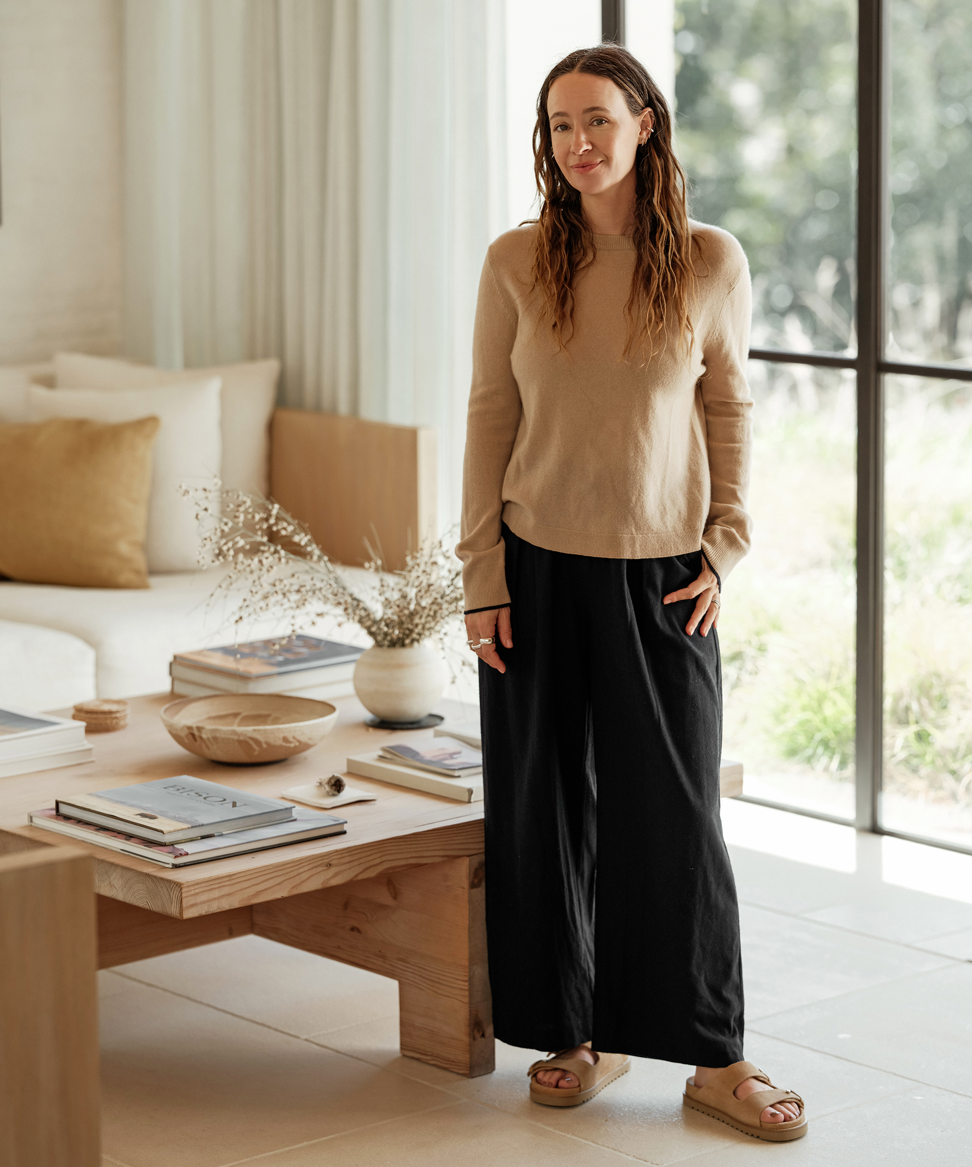 jenni standing in her family room wearing an oatmeal cashmere crewneck and navy trousers