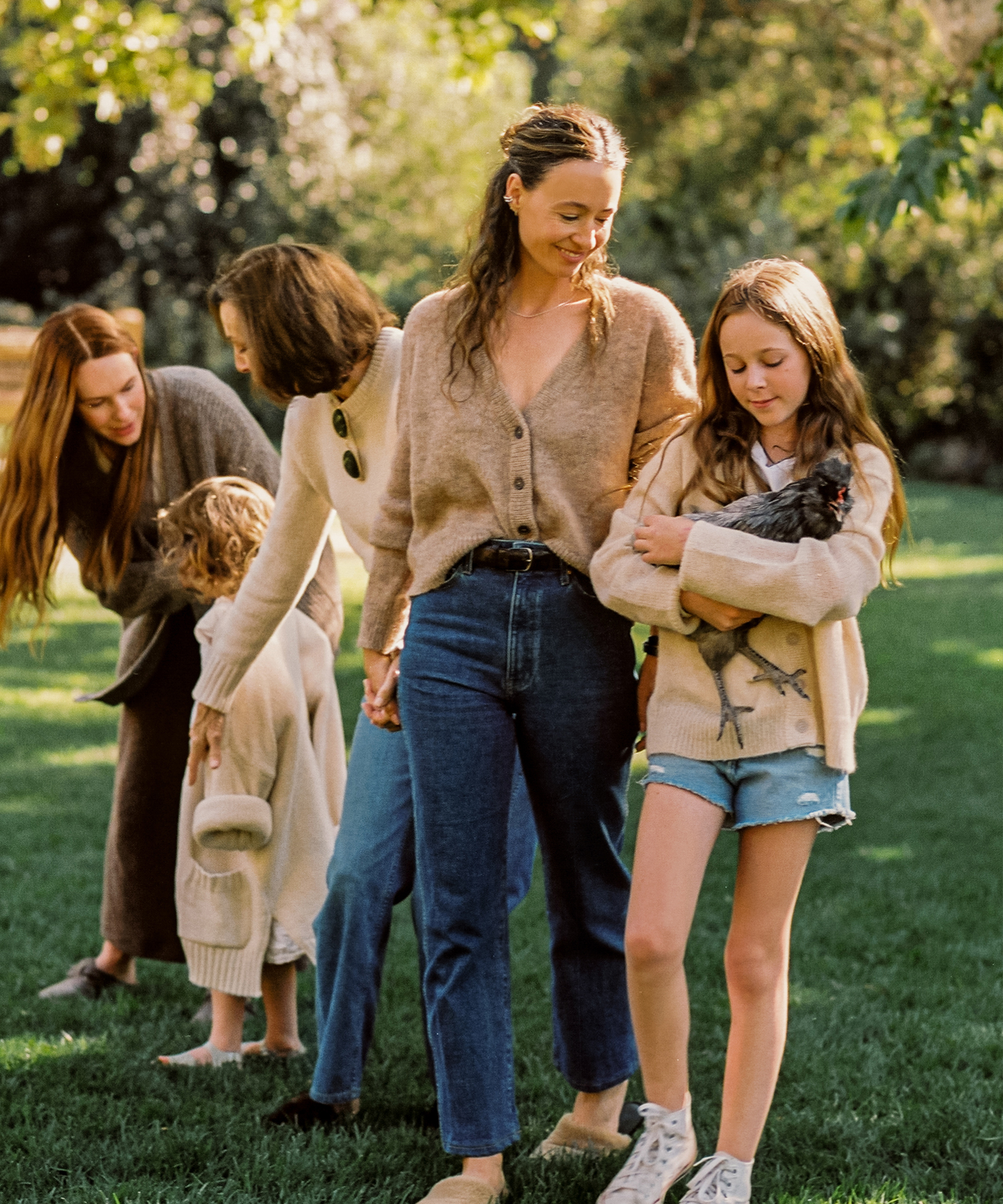 jenni with her daughter and mother and sister in the backyard wearing blue jeans and a taupe cardigan
