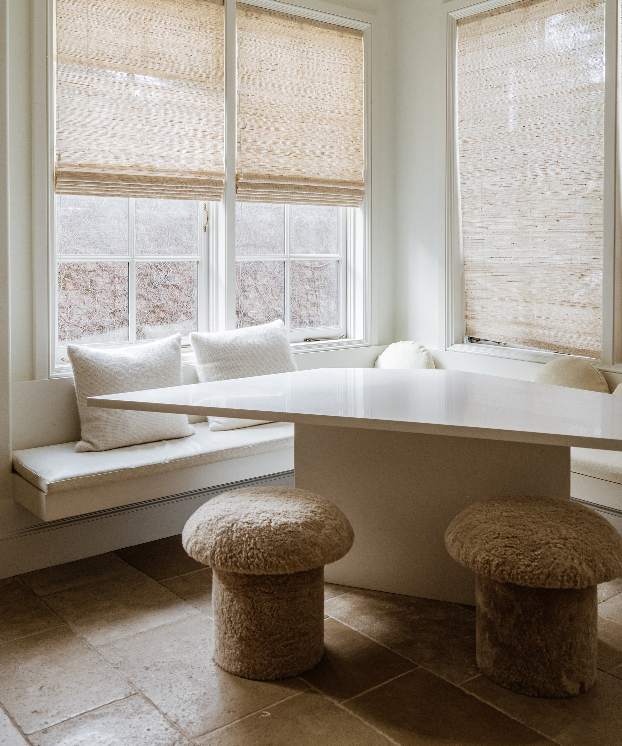 a kitchen nook with a creme dining table and two taupe mushroom stools with a built in bench