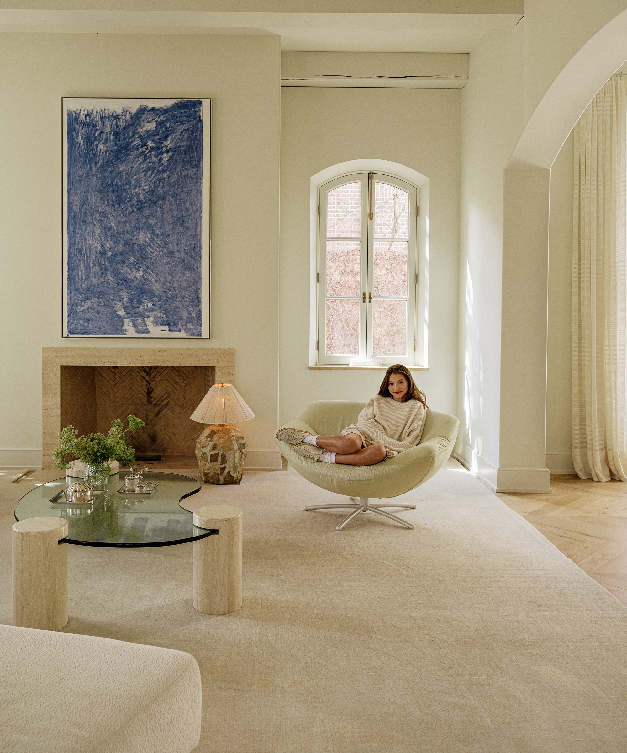 an ivory plush area rug with a leather accent chair next to a stone mantle with a large blue abstract painting