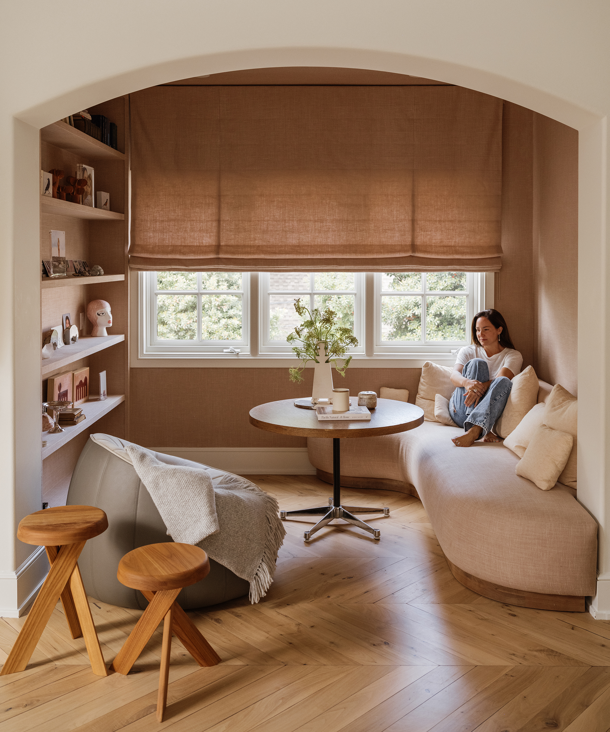 a reading nook with a built in upholstered pale pink bench with matching pillows next to a round table and built in bookshelf