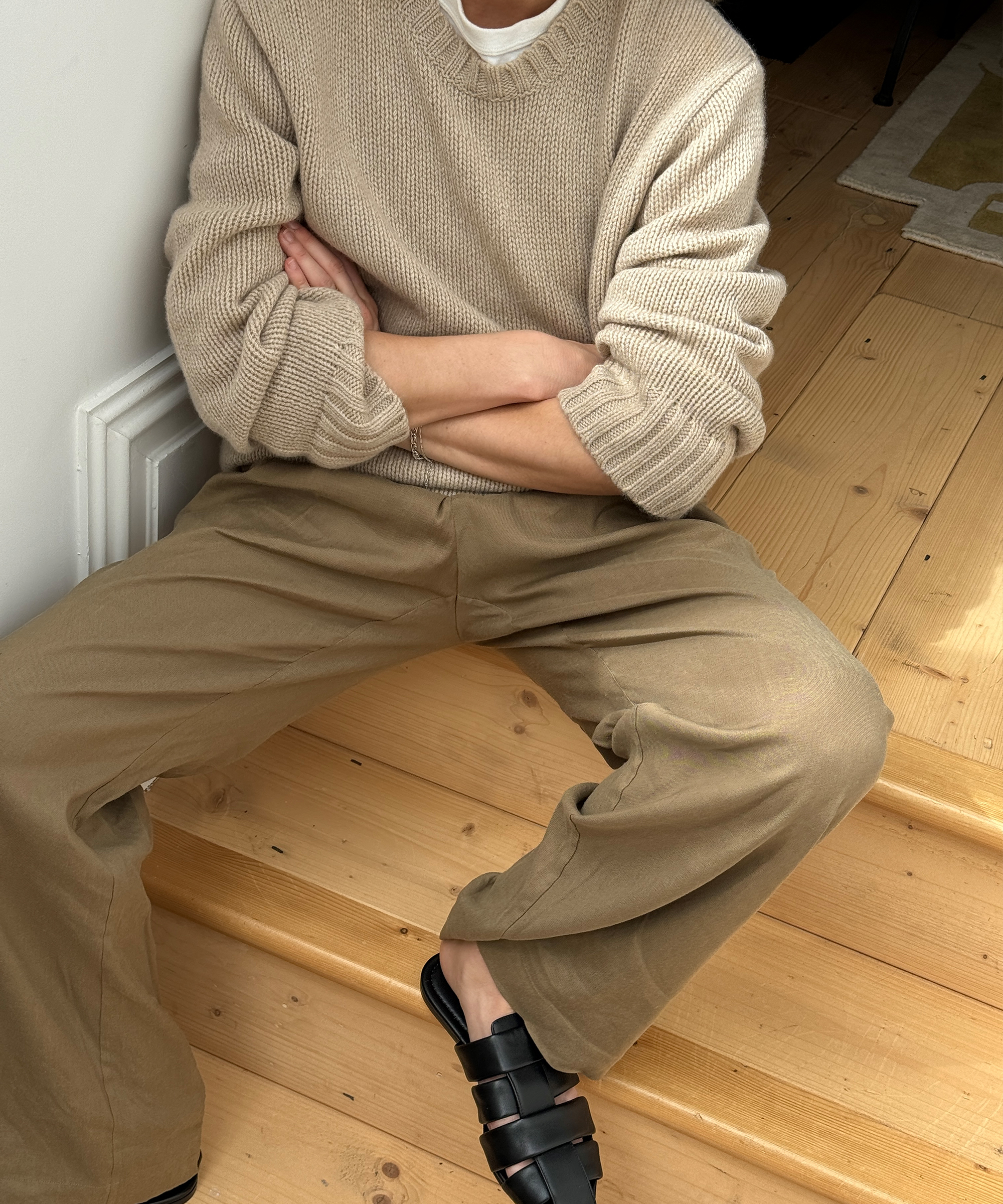 lucy sitting on wooden stairs in a taupe cashmere crewneck sweater and khaki pants with black fisherman mules
