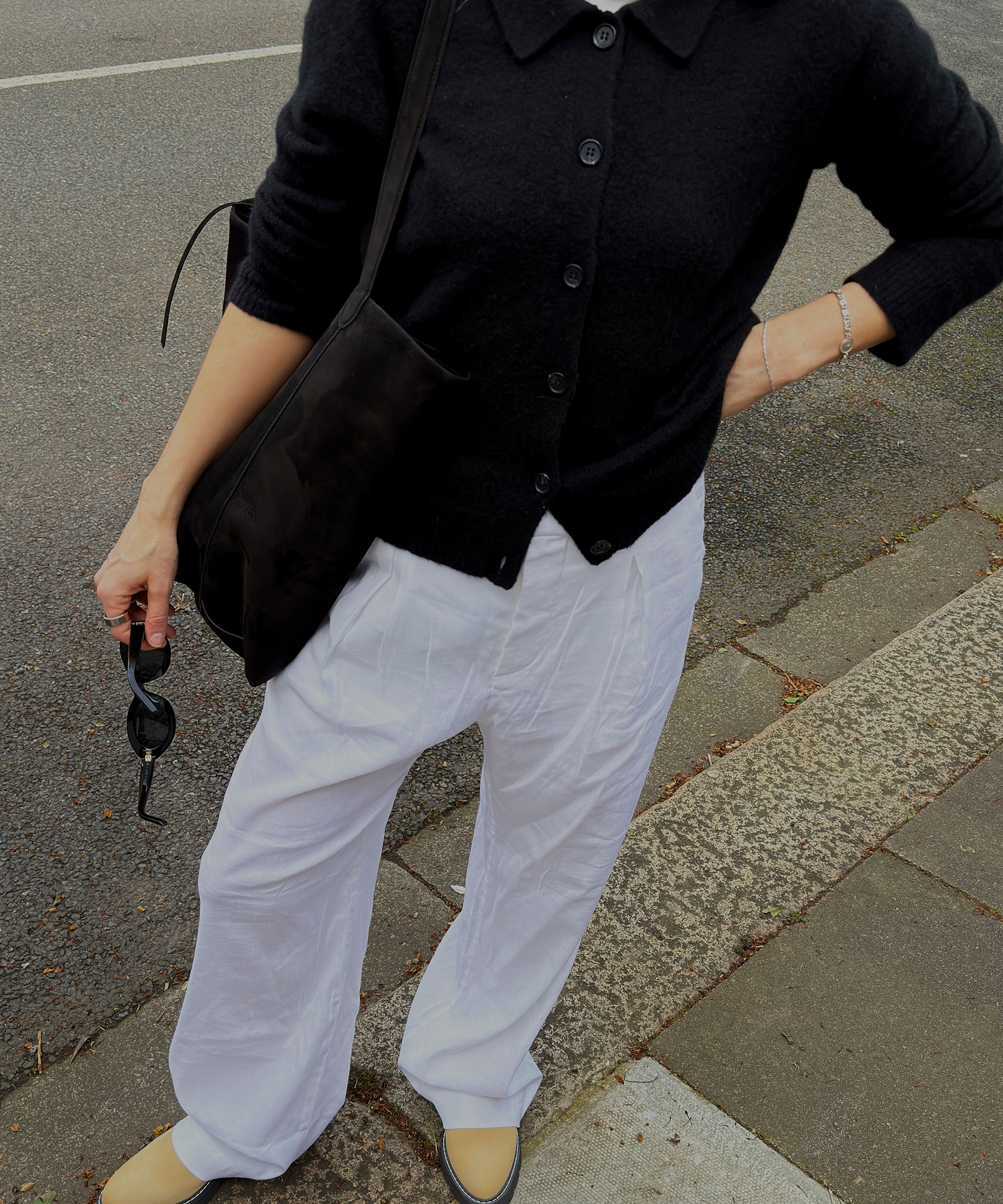 lucy williams in white linen trousers and a black cardigan standing in the street