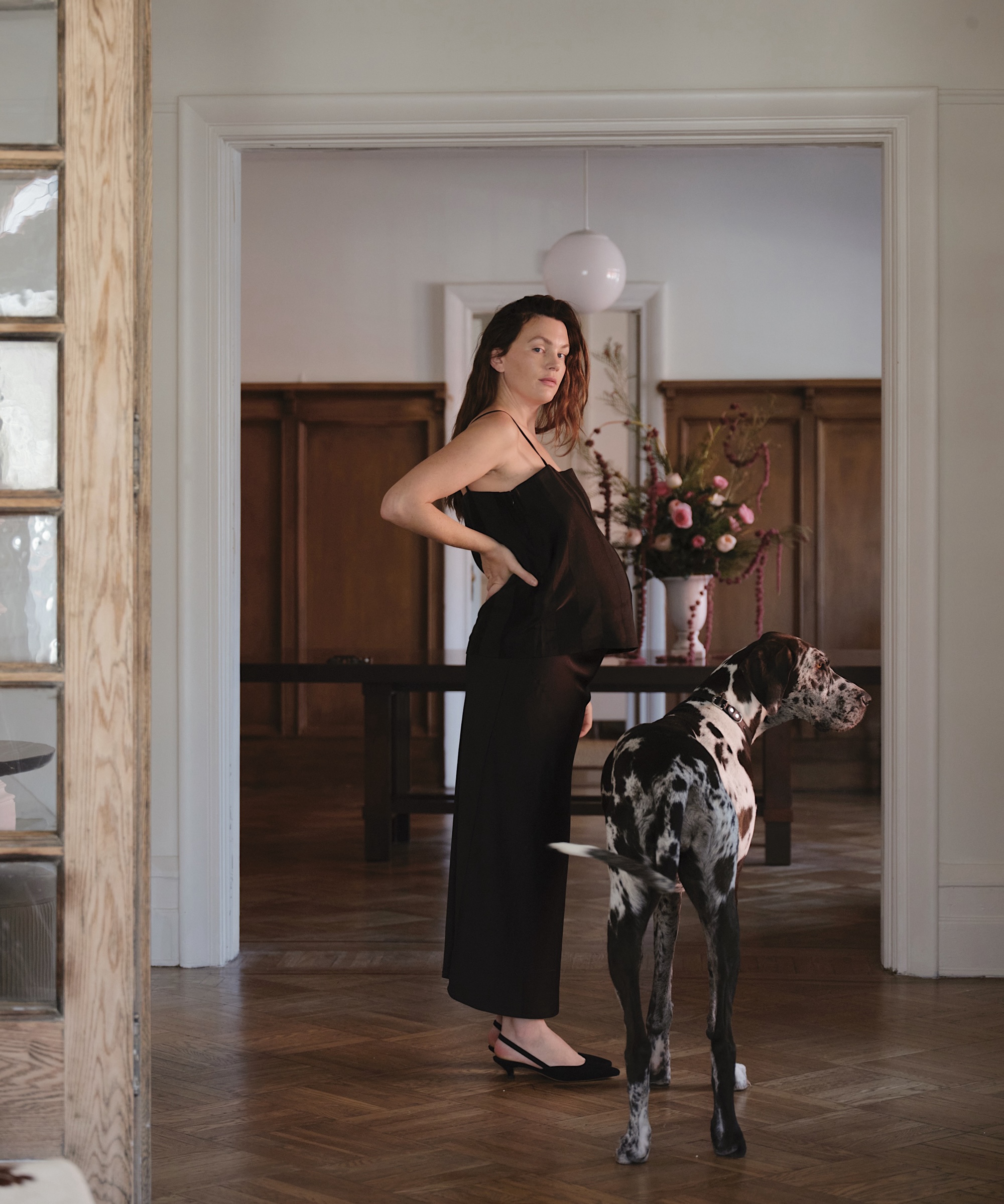 madelynn in a black slik tank and black maxi skirt standing next to her dog in a hallway