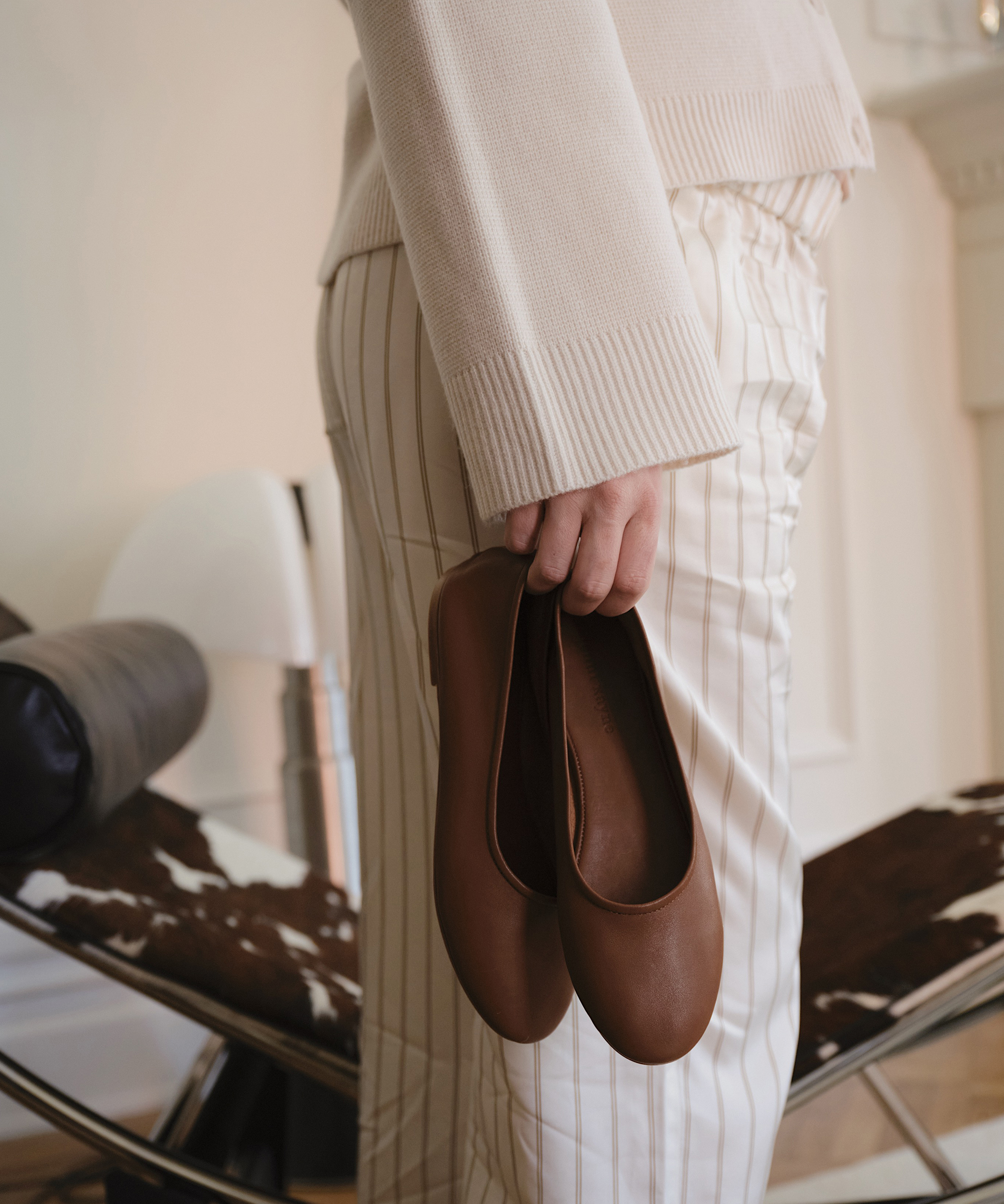 madelynn hudson holding a pair of saddle ballet flats with a pair of striped pants and an ivory sweater