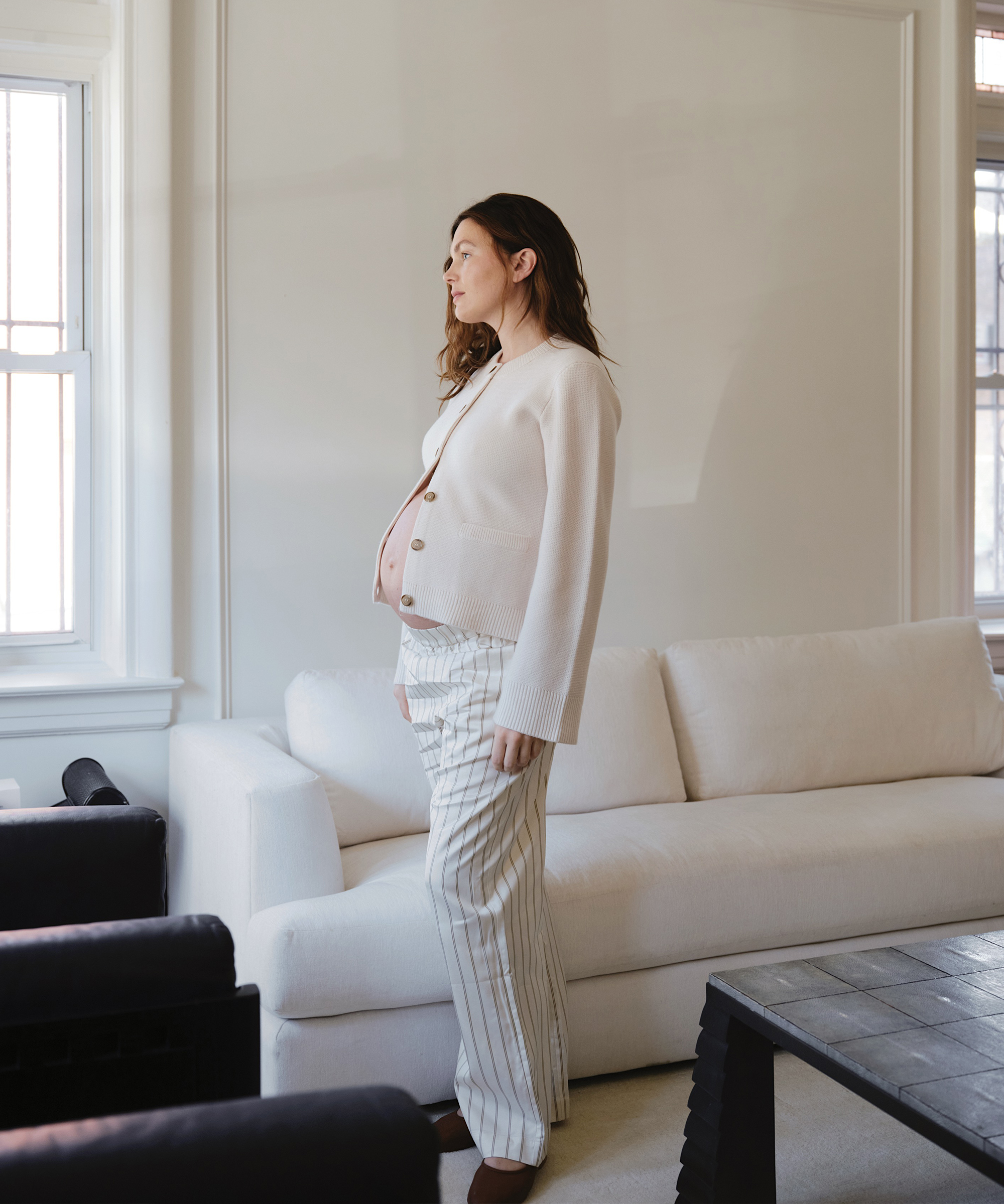 madelynn standing in her living room next to a white couch in striped pants and an ivory cooper cardigan