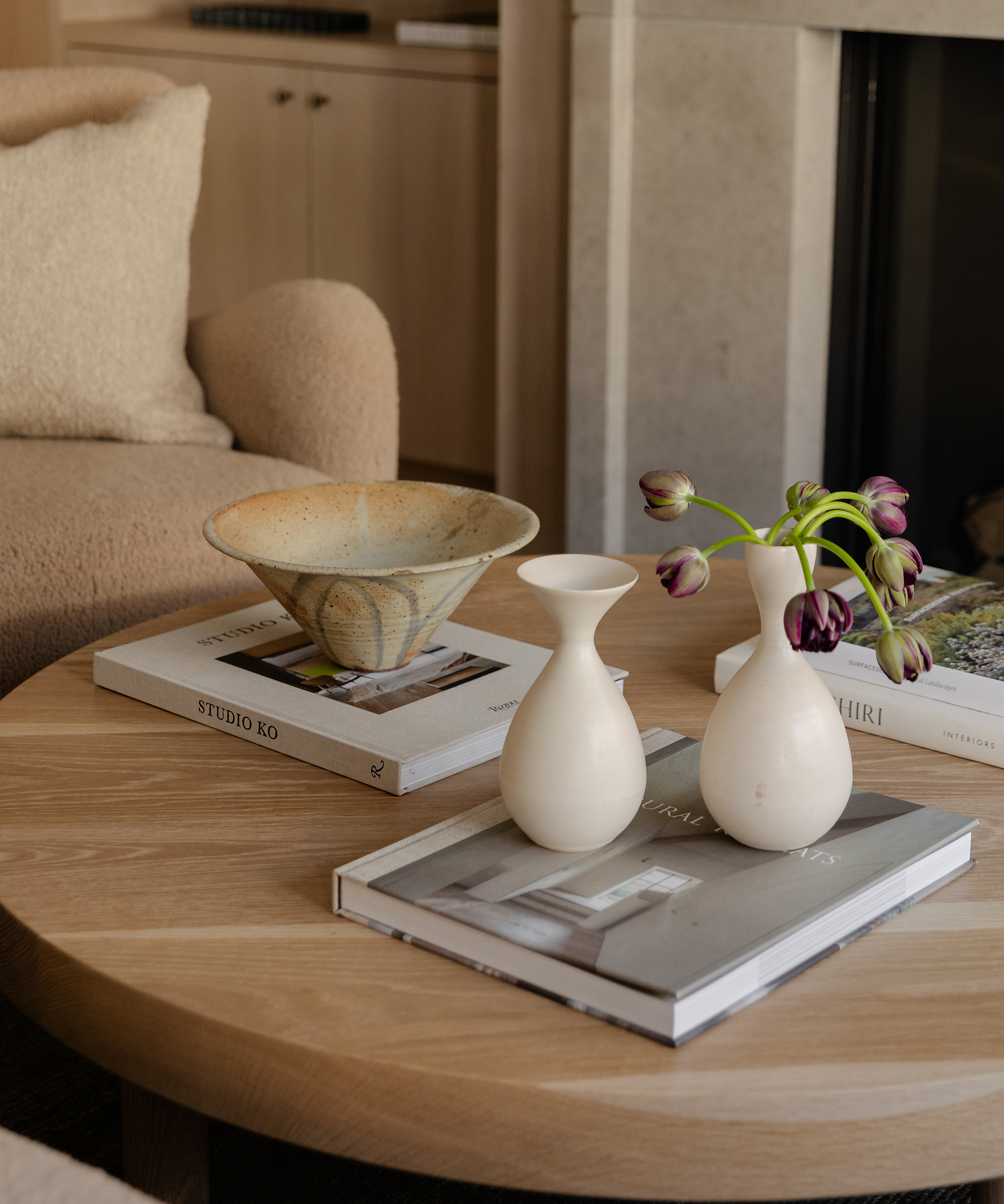 a wood round coffee table with coffee table book two ivory vases and a decorative bowl